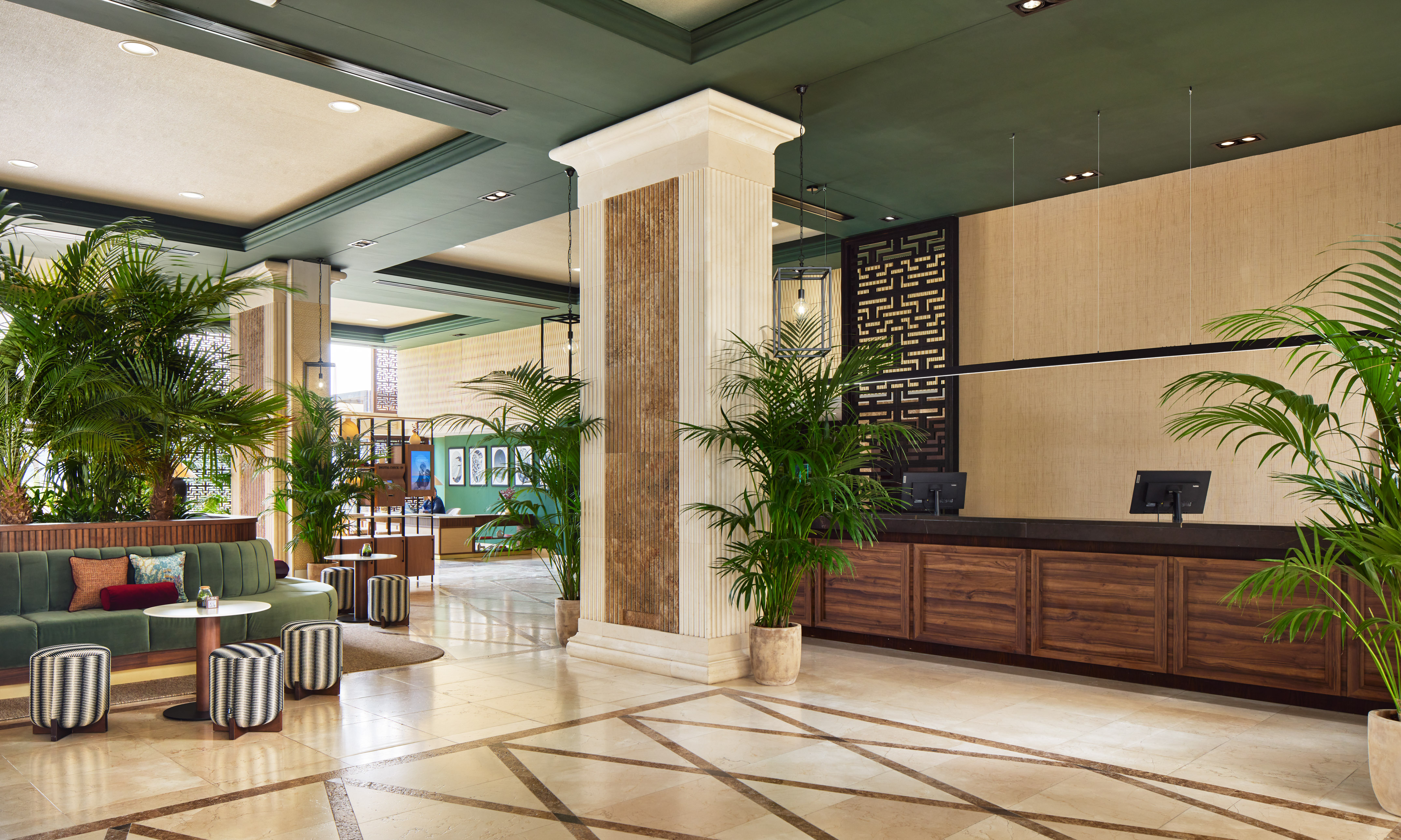 Elegant hotel lobby with green sofa, palm plants, and modern reception desk.