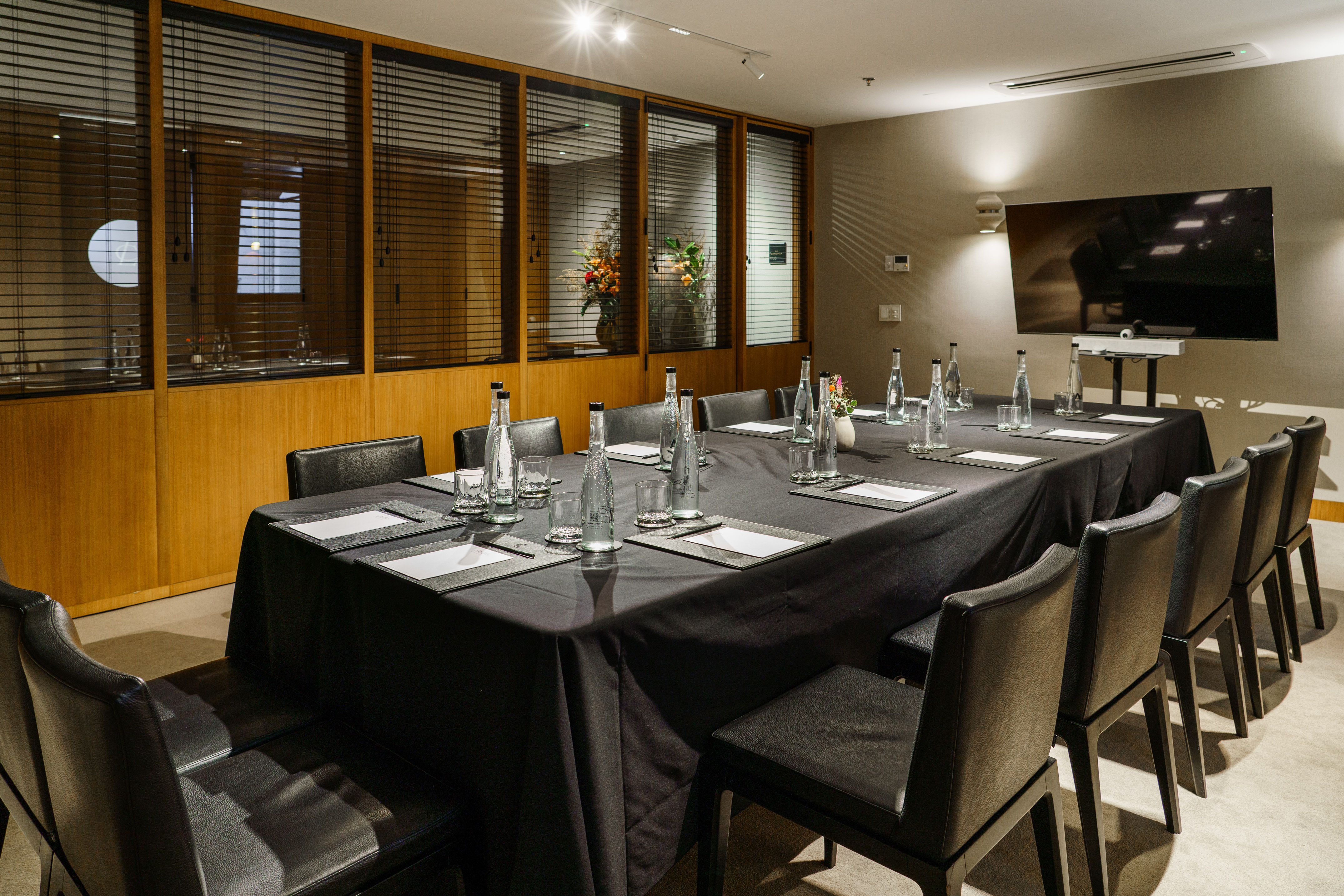 Modern meeting room with black table, leather chairs, and large display.