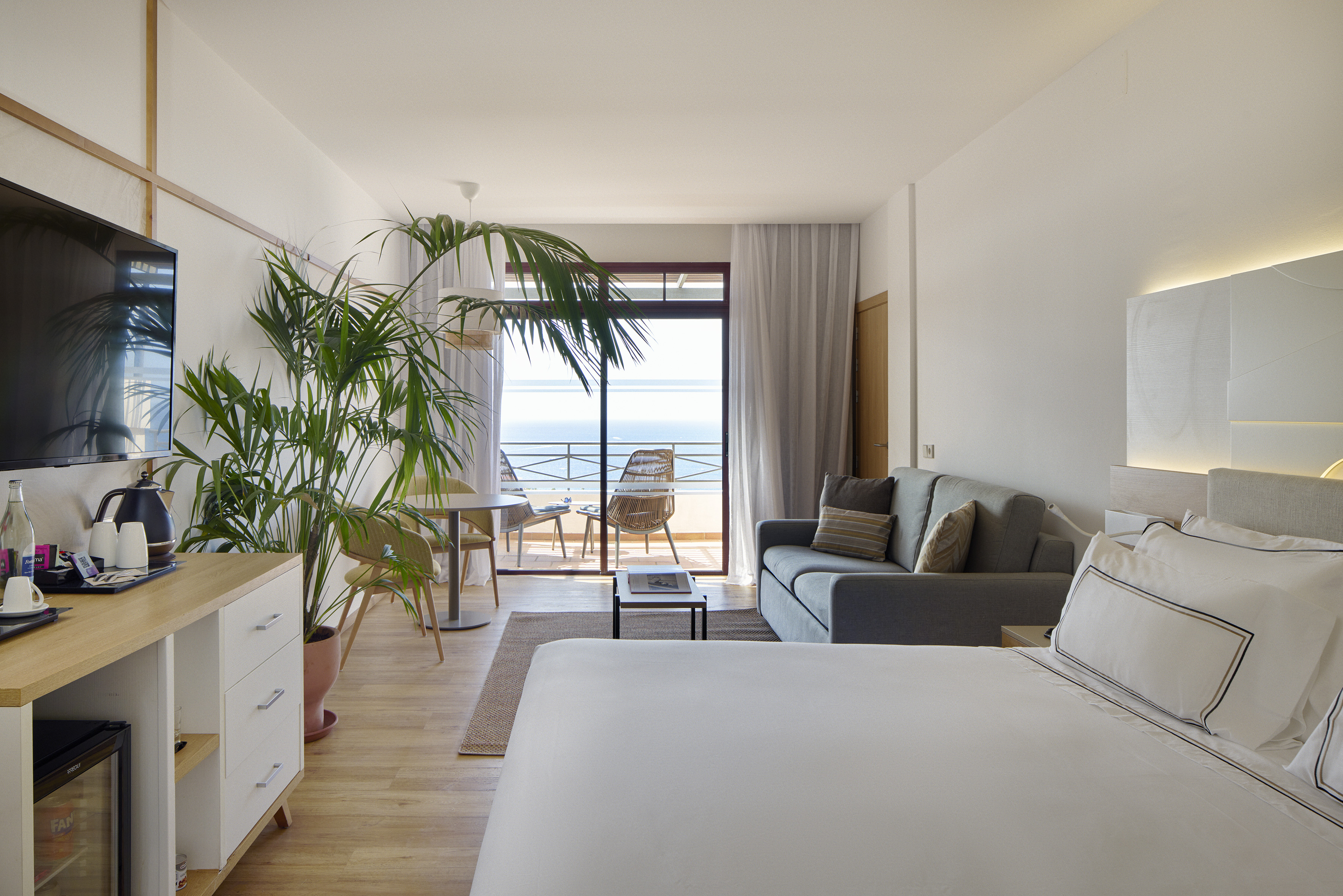 Modern hotel room with sea view balcony, bed, and living area.