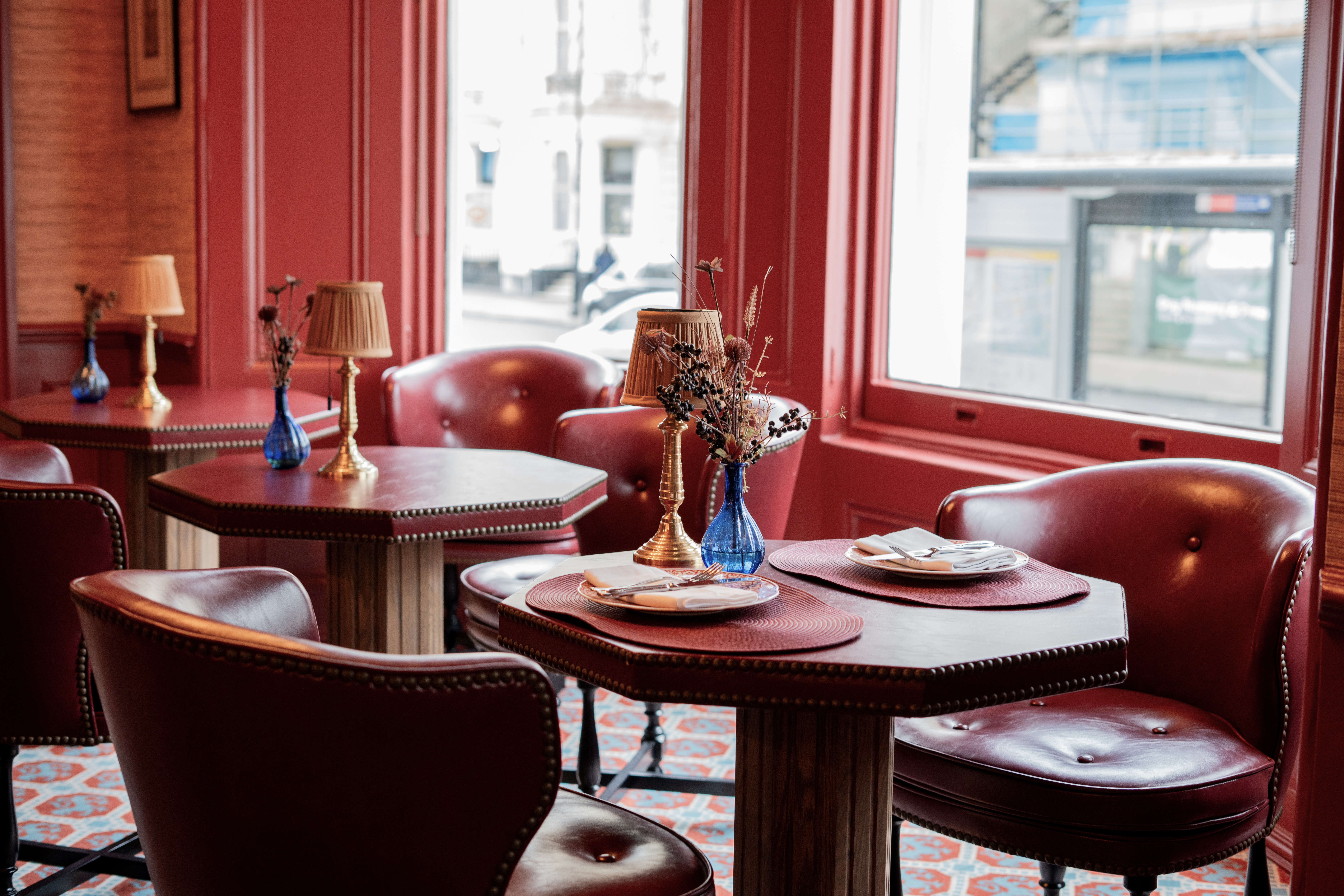 Cozy red cafe interior: leather chairs, small tables, lamps, street view.