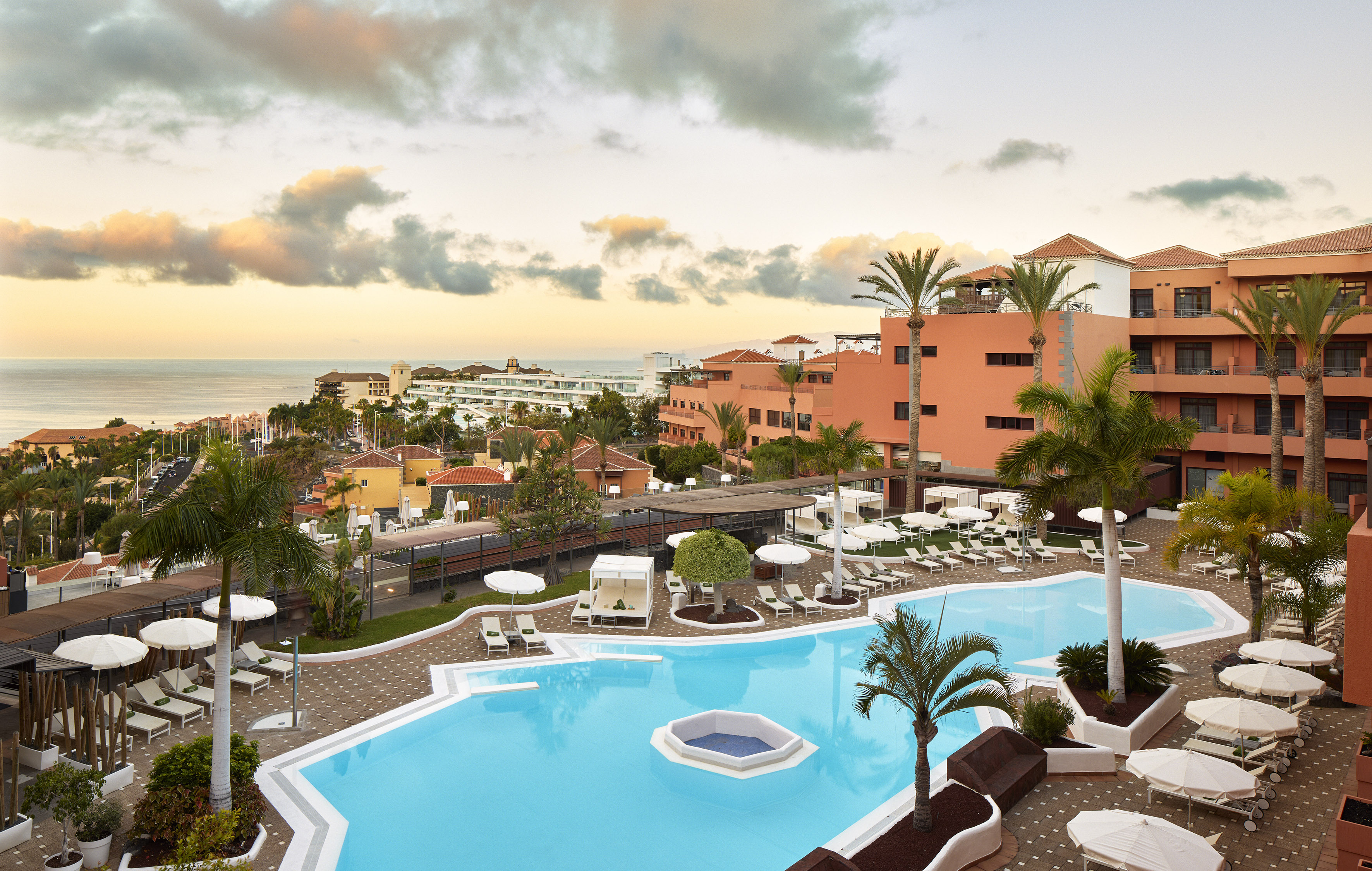 Tropical resort with swimming pools, palm trees, and sunset ocean view.