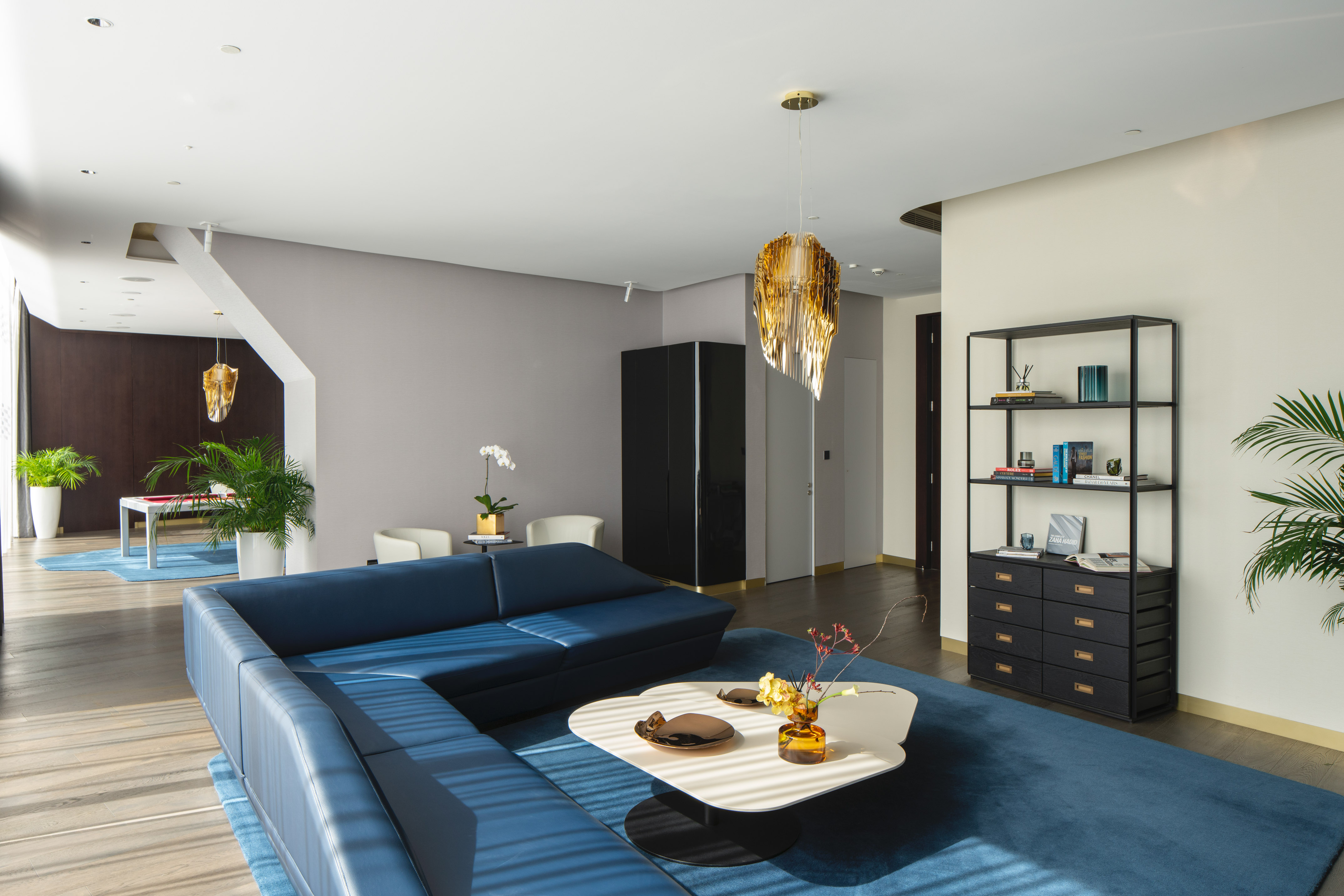 Modern living room with blue sectional sofa, white coffee table, and gold chandelier.