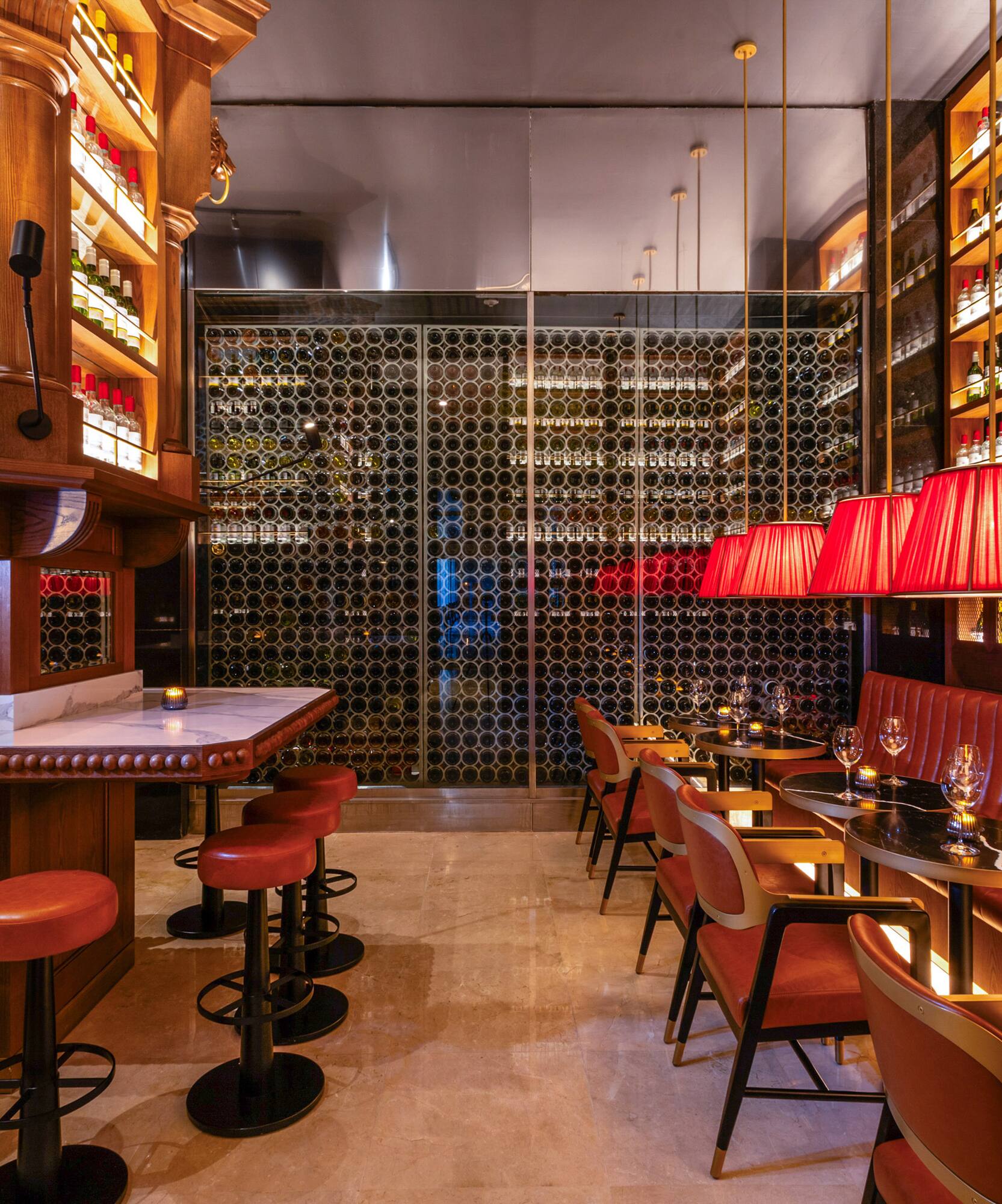 Bar con botellas, taburetes rojos, lámparas y bodega de vinos.