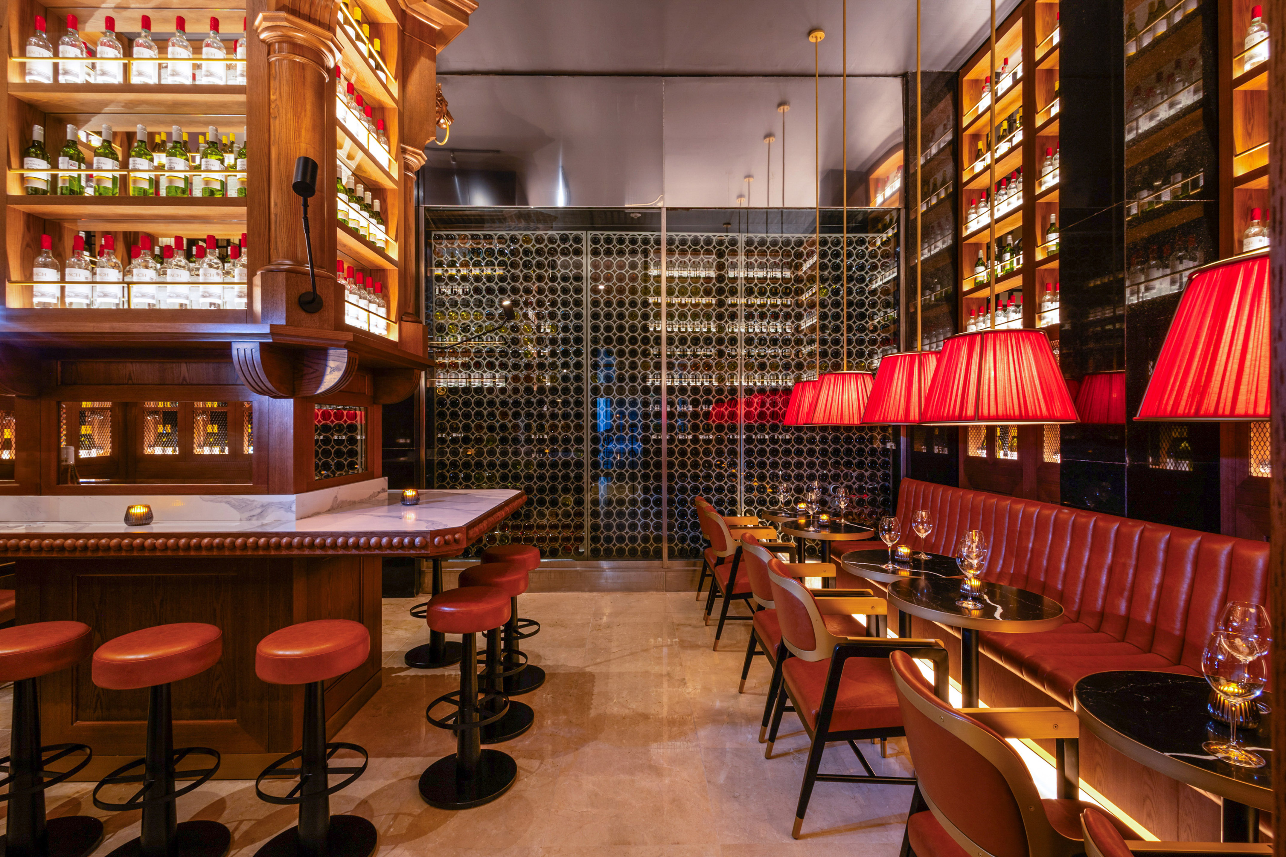 Bar con botellas, taburetes rojos, lámparas y bodega de vinos.