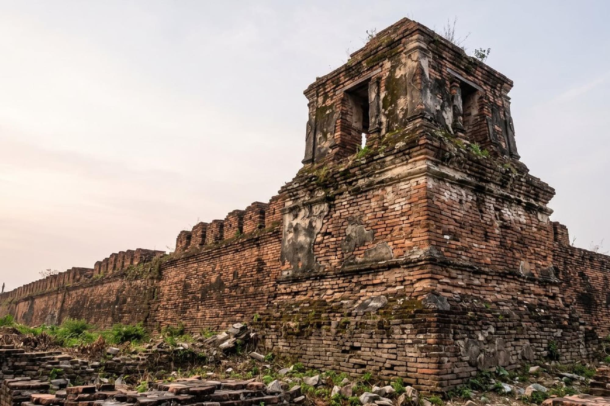 Ayutthaya brick fortress wall ruins with corner tower, overgrown with moss.