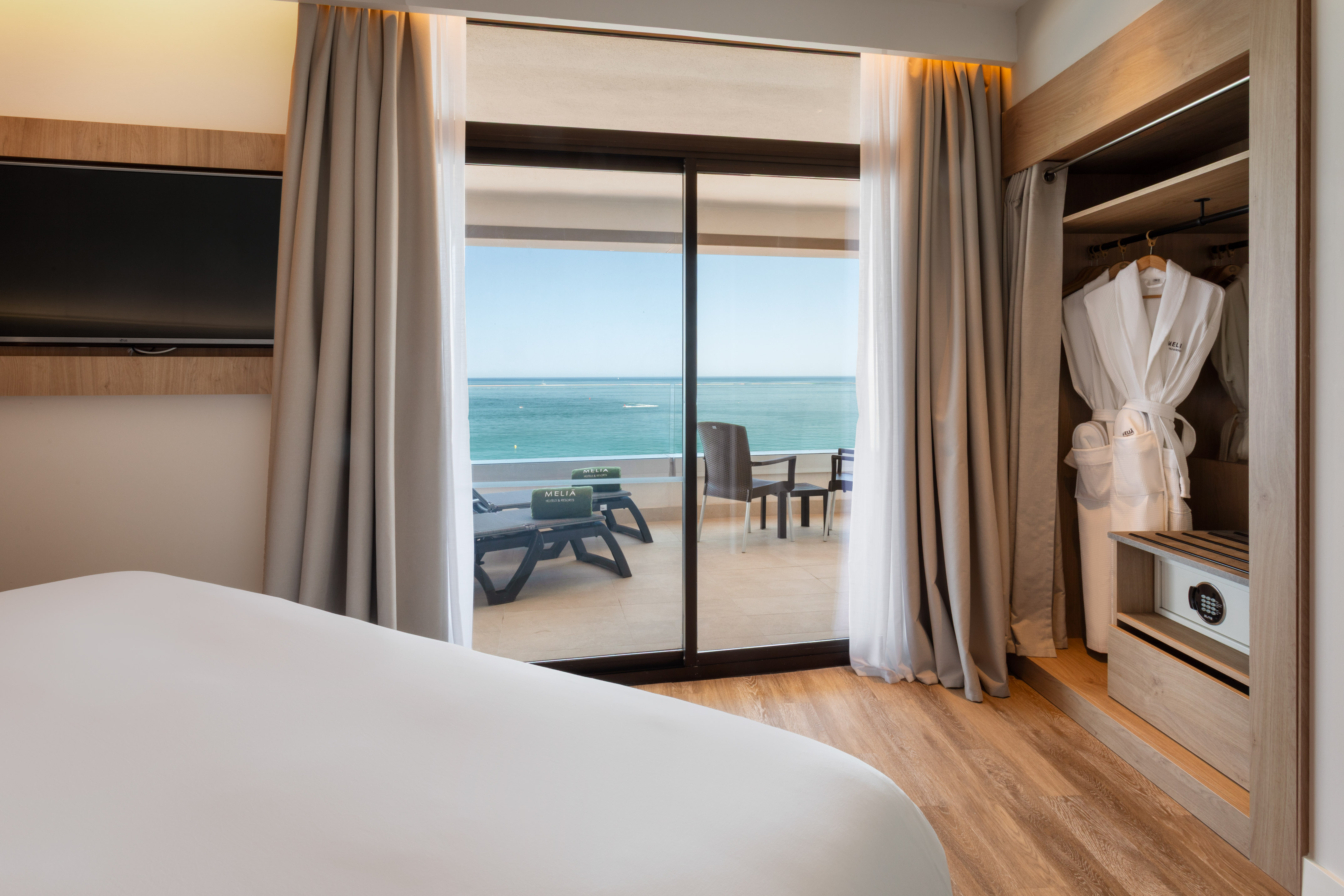 Modern hotel bedroom with ocean view balcony, bed, TV, and wardrobe.