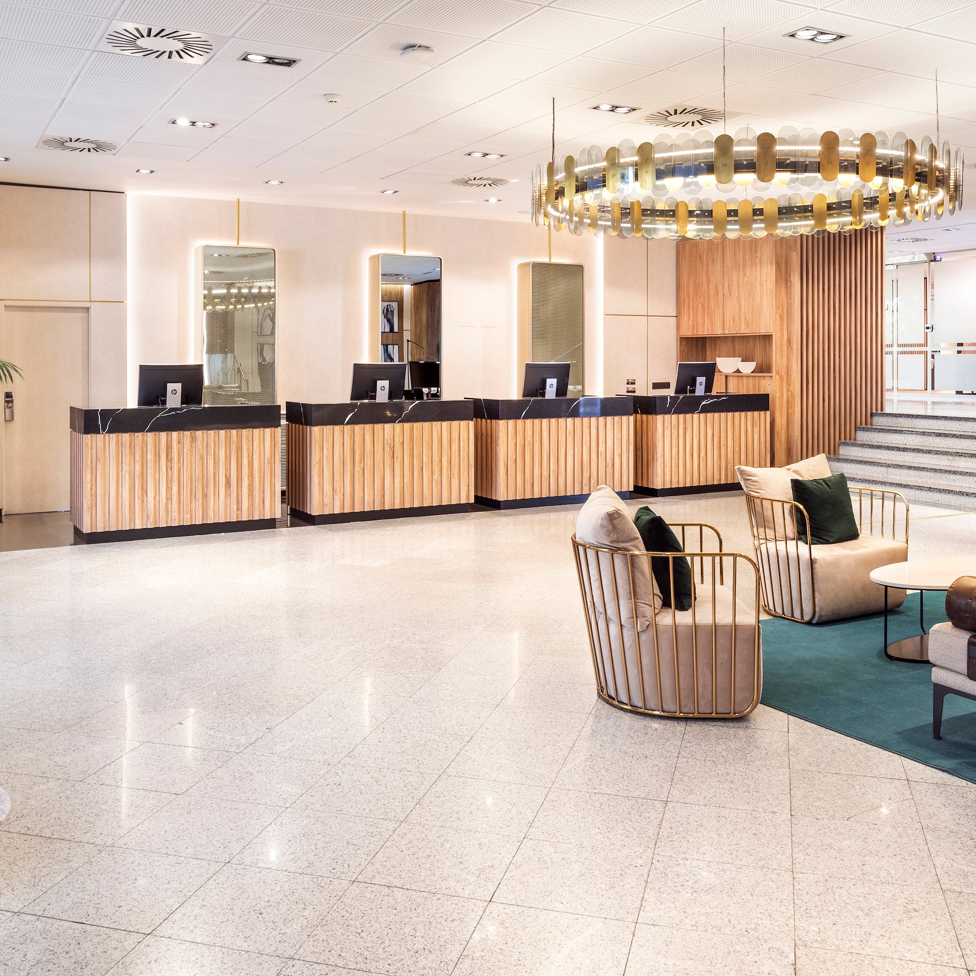Modern hotel lobby with wood reception desks, lounge area, and stylish chandelier.