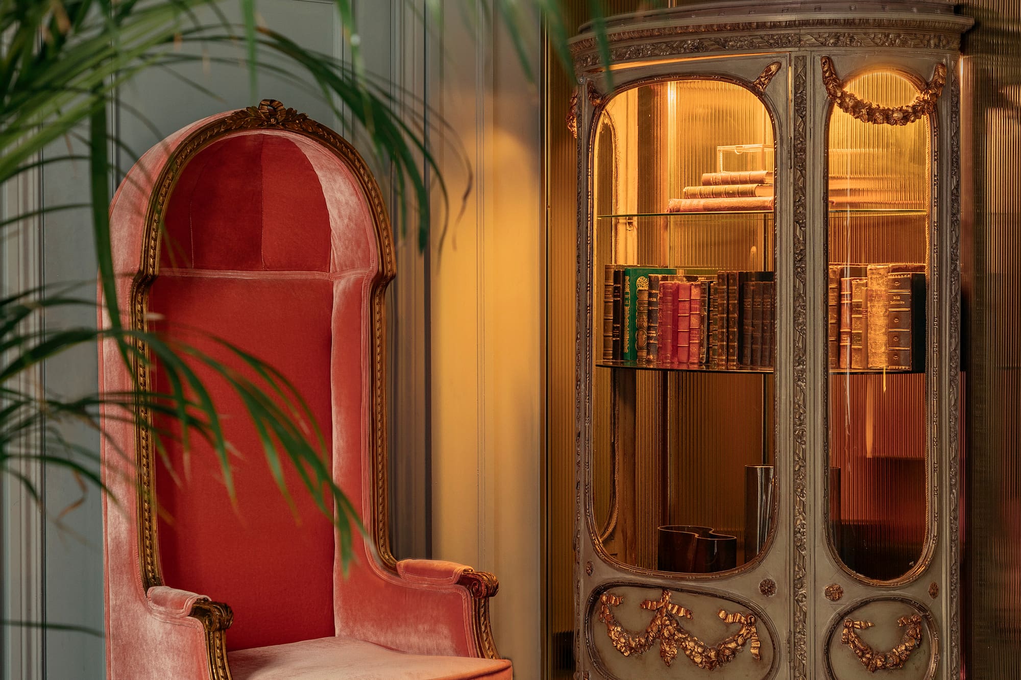 Vintage coral velvet armchair, ornate gold display cabinet with antique books.