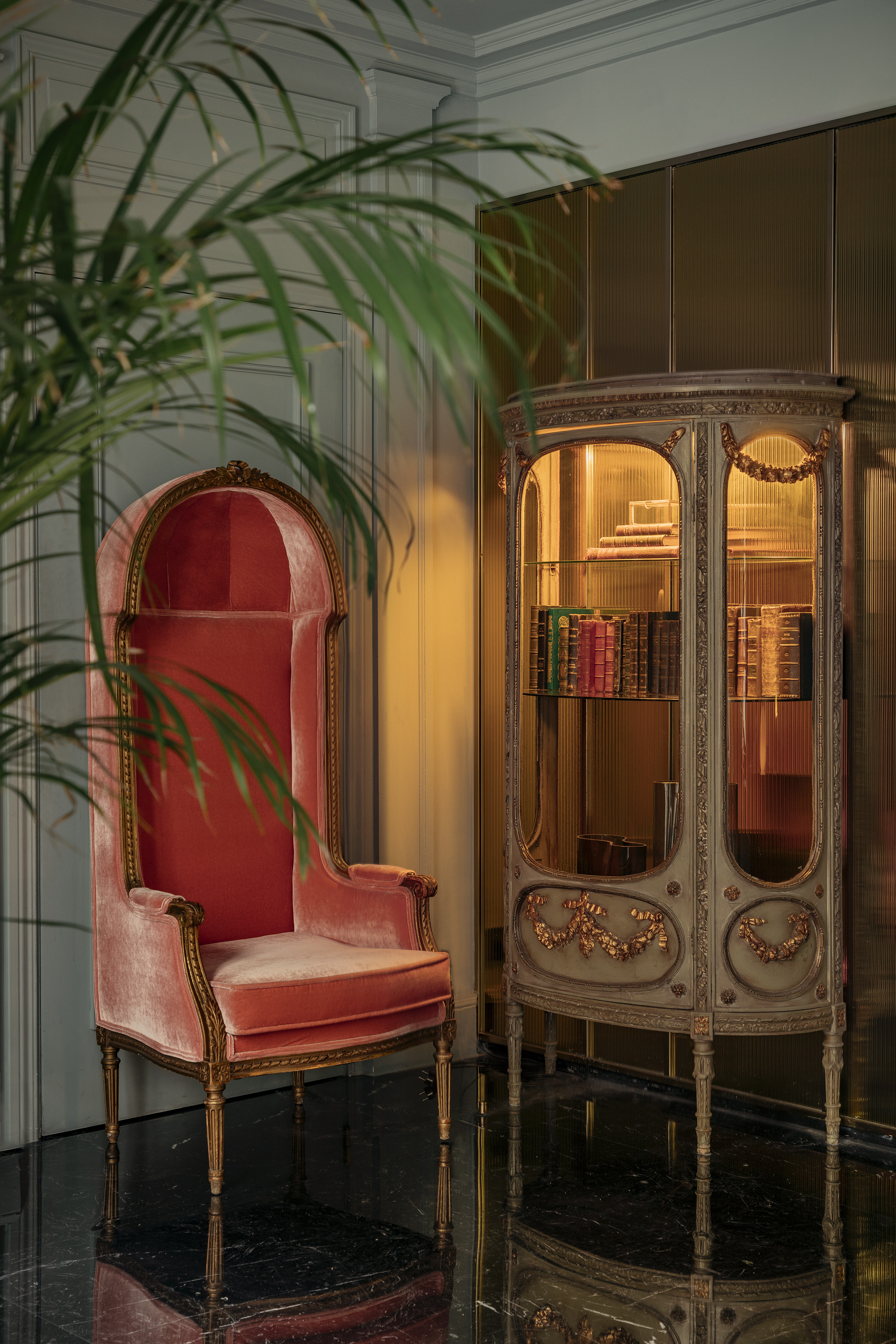 Vintage coral velvet armchair, ornate gold display cabinet with antique books.