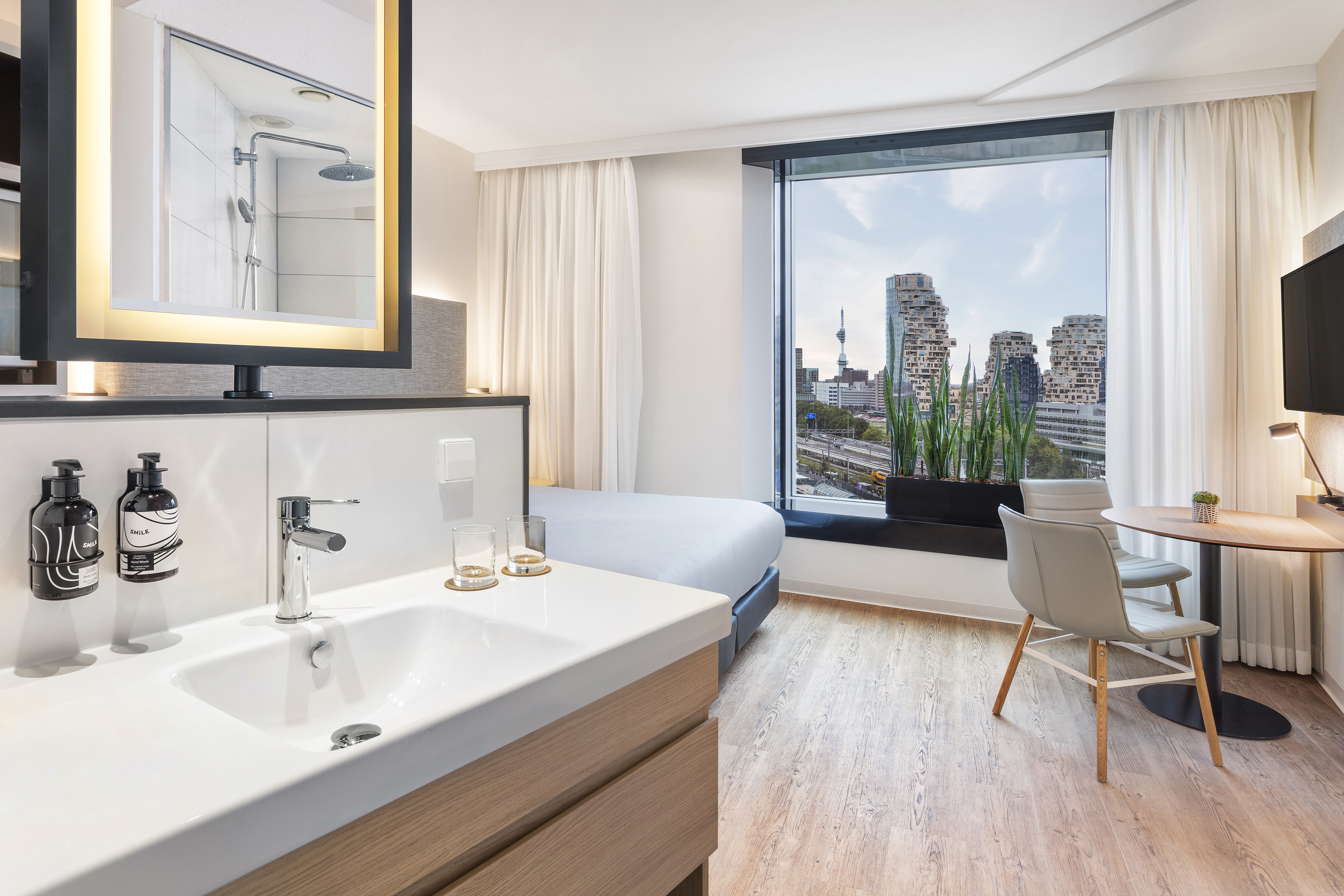 Sleek hotel room featuring a city view, bed, modern vanity, and work area.