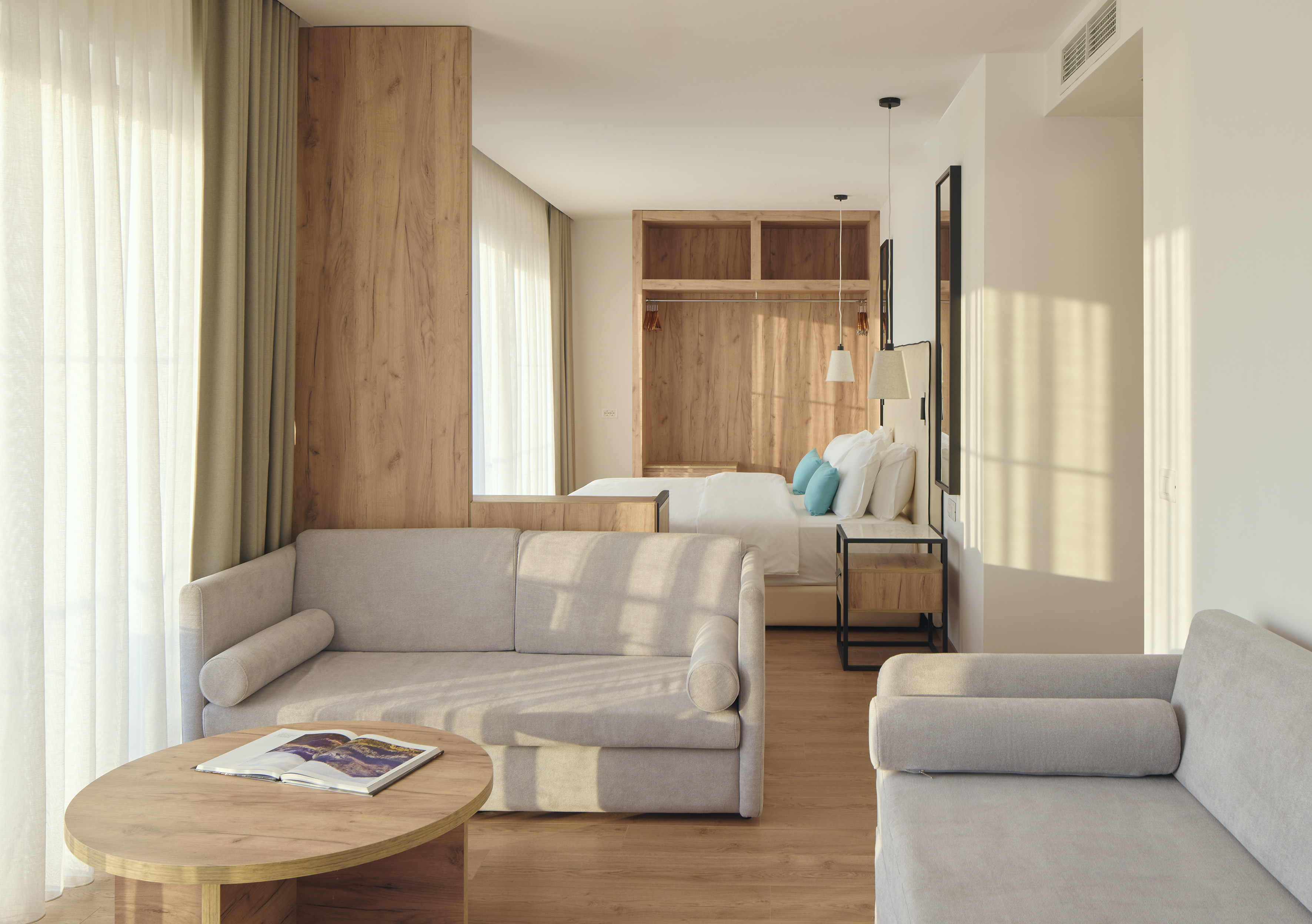 Bright modern hotel suite with sofa, wooden details, and minimalist bedroom.