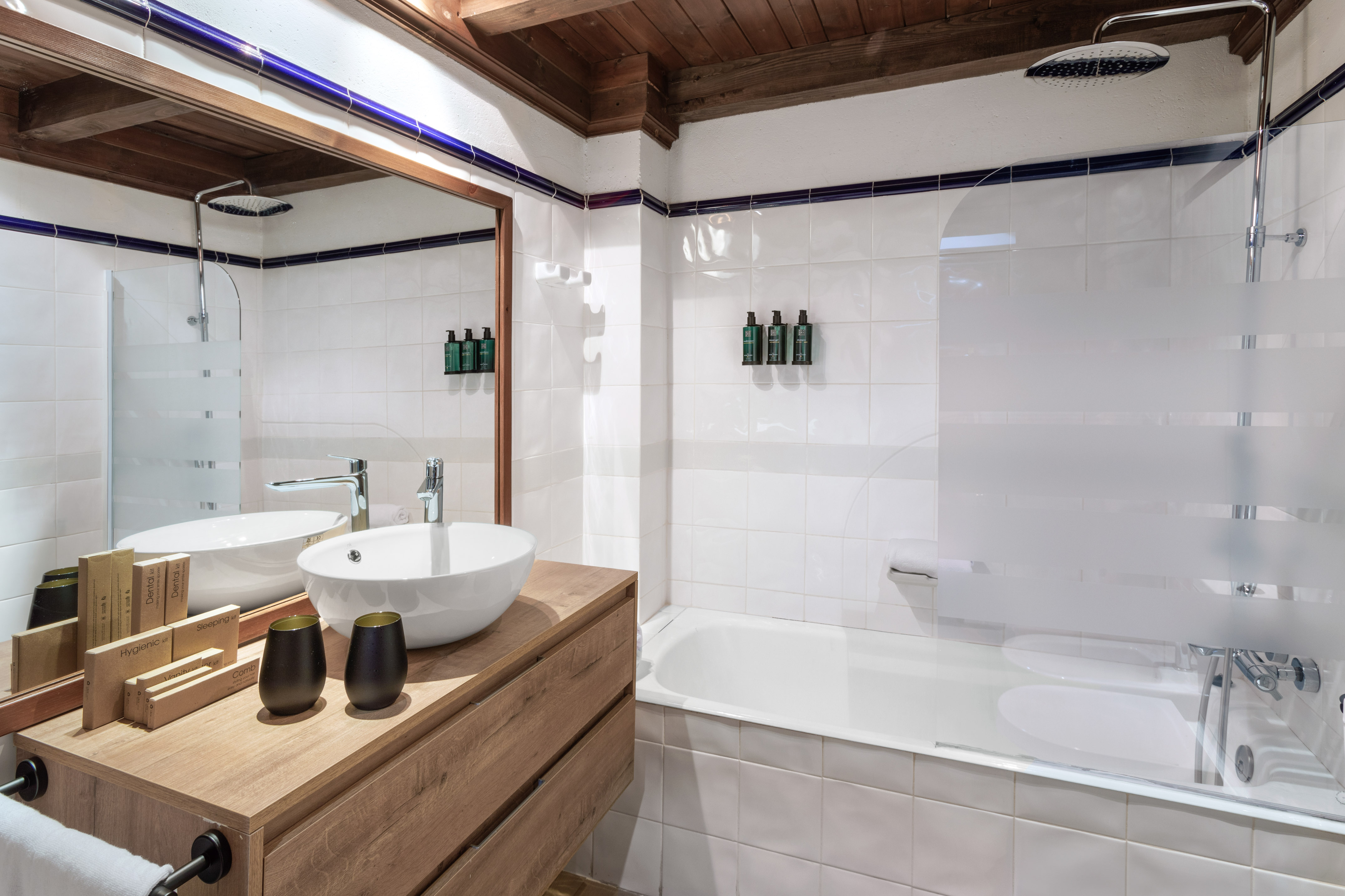 Modern bathroom with white tiles, wood vanity, vessel sink, bathtub, and rain shower.