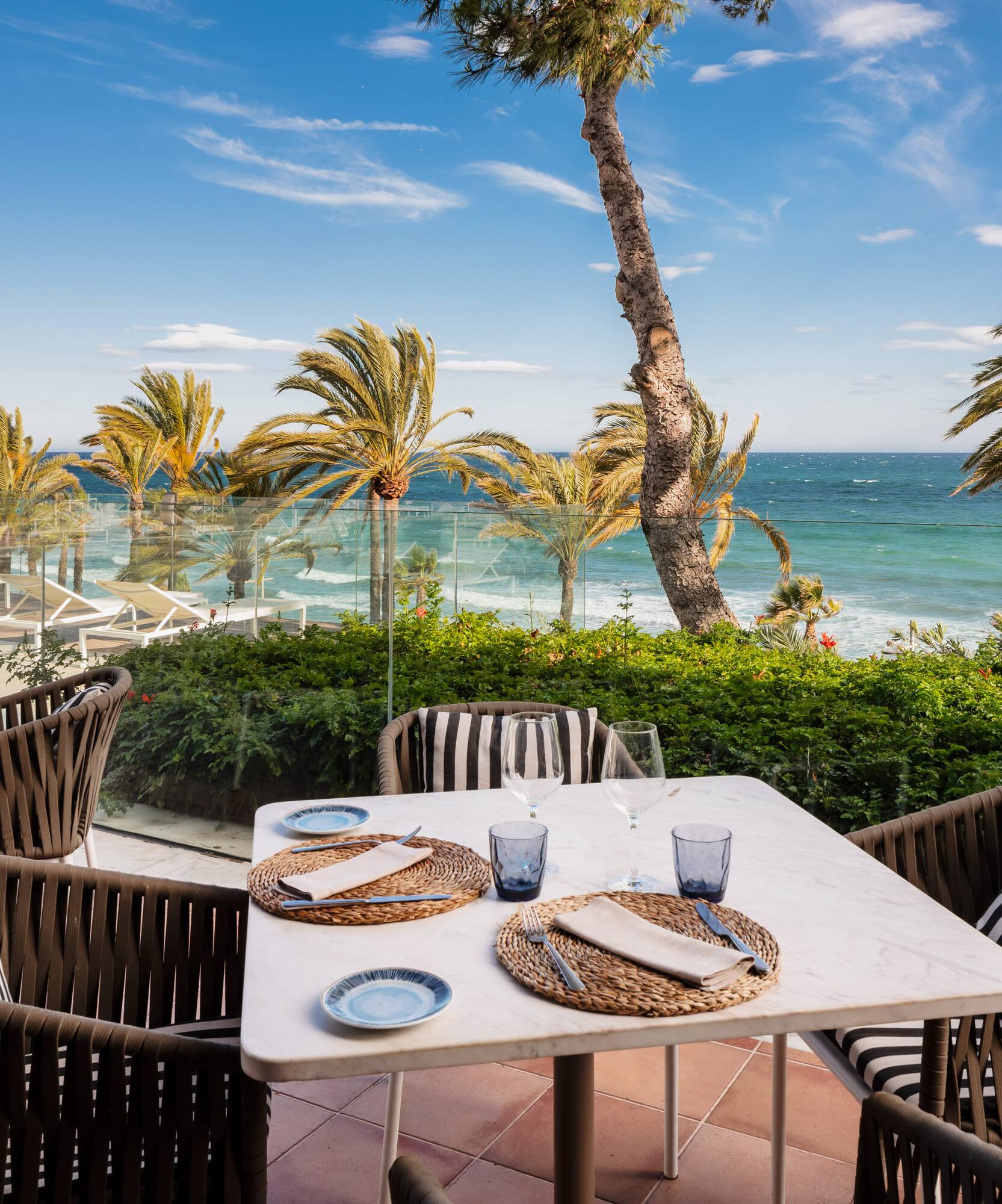 Tropical resort patio with palm trees, lounge chairs, and turquoise ocean.