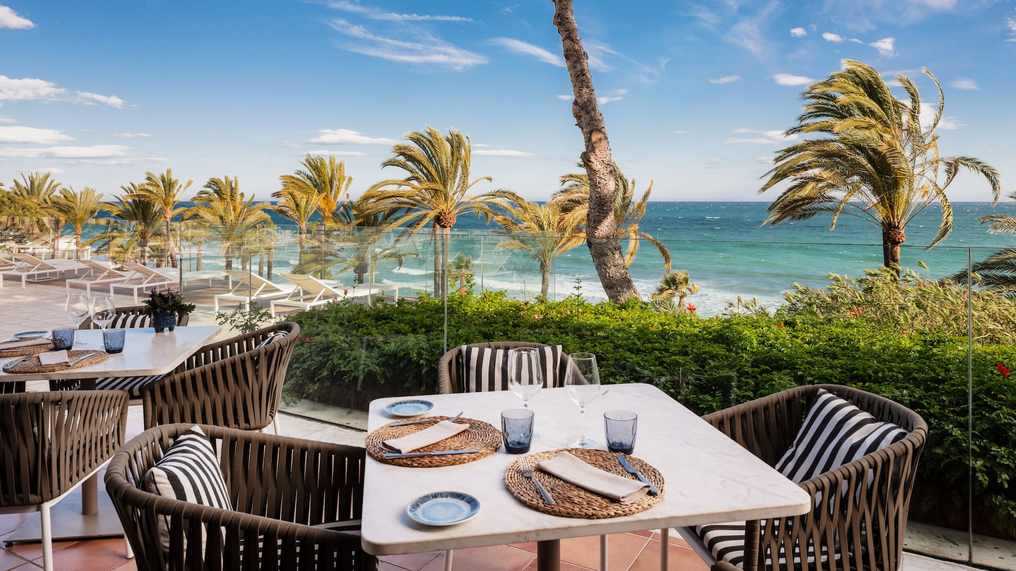 Tropical beach resort with palm trees, white lounge chairs, and blue ocean.