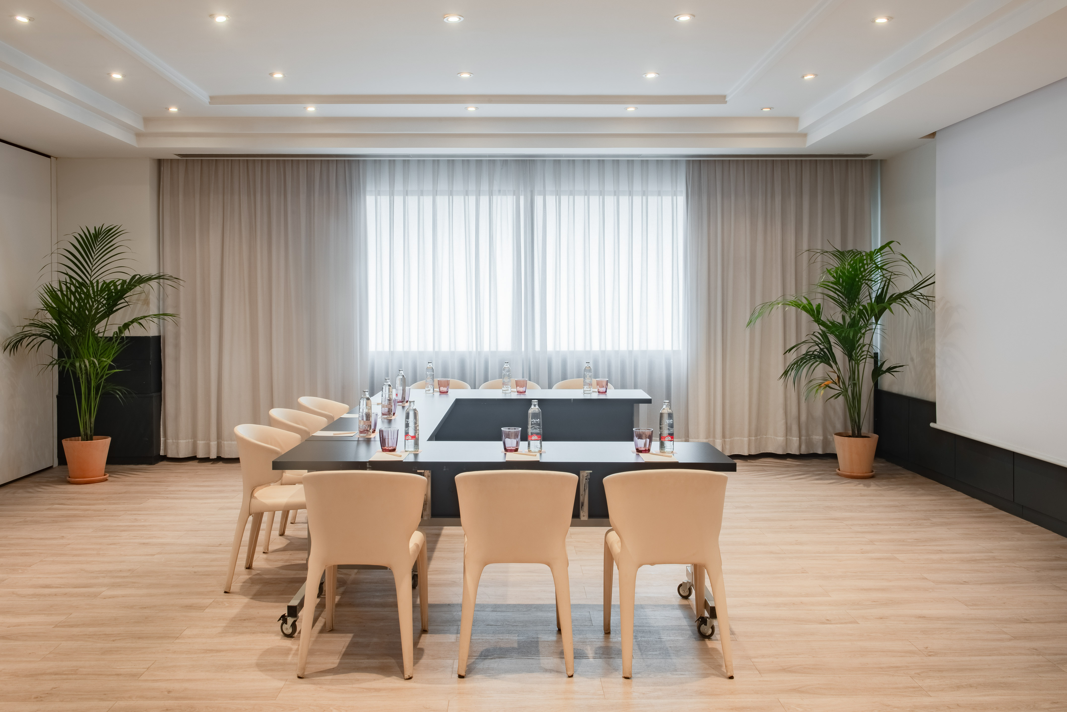 Modern conference room with U-shaped table, beige chairs, and plants.