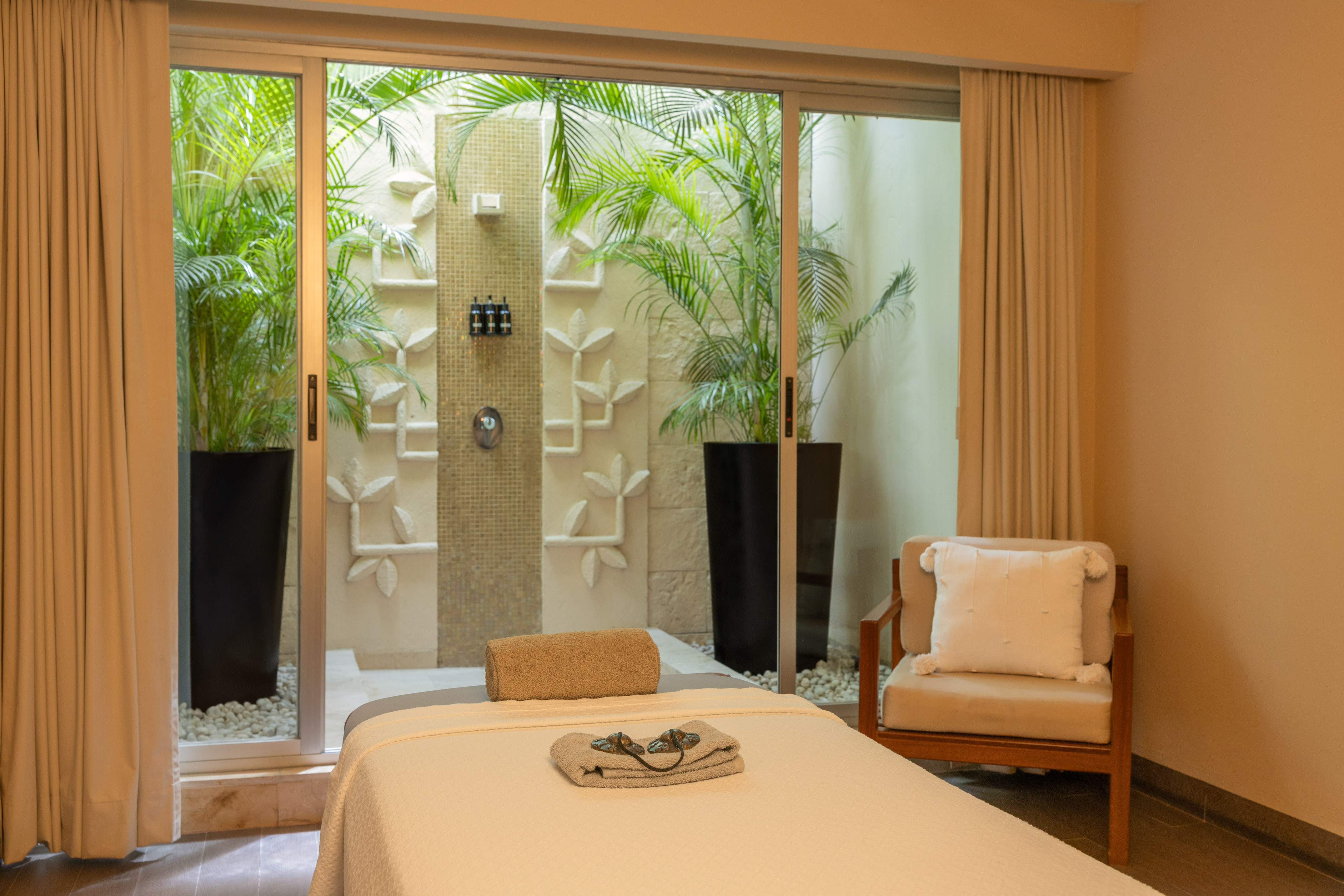 Luxury spa massage room with outdoor shower, tropical plants, and elegant decor.