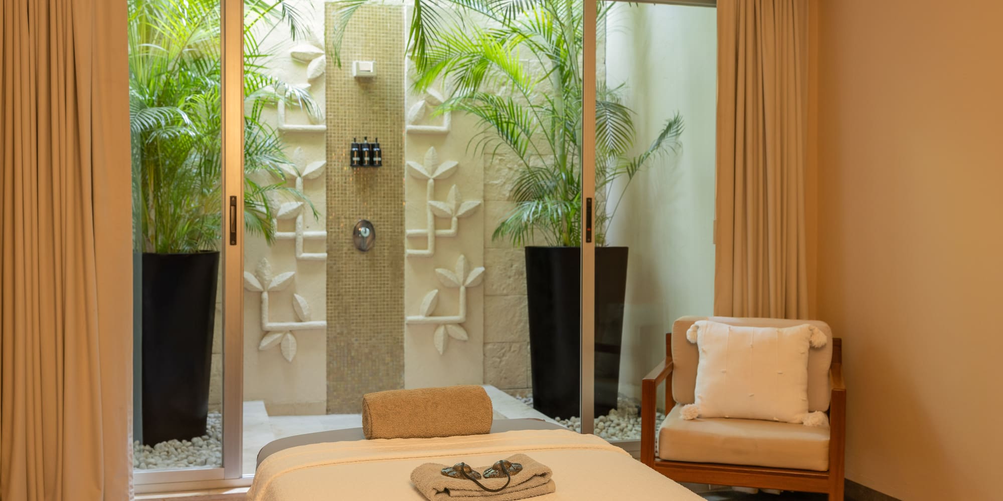 Luxury spa massage room with outdoor shower, tropical plants, and elegant decor.