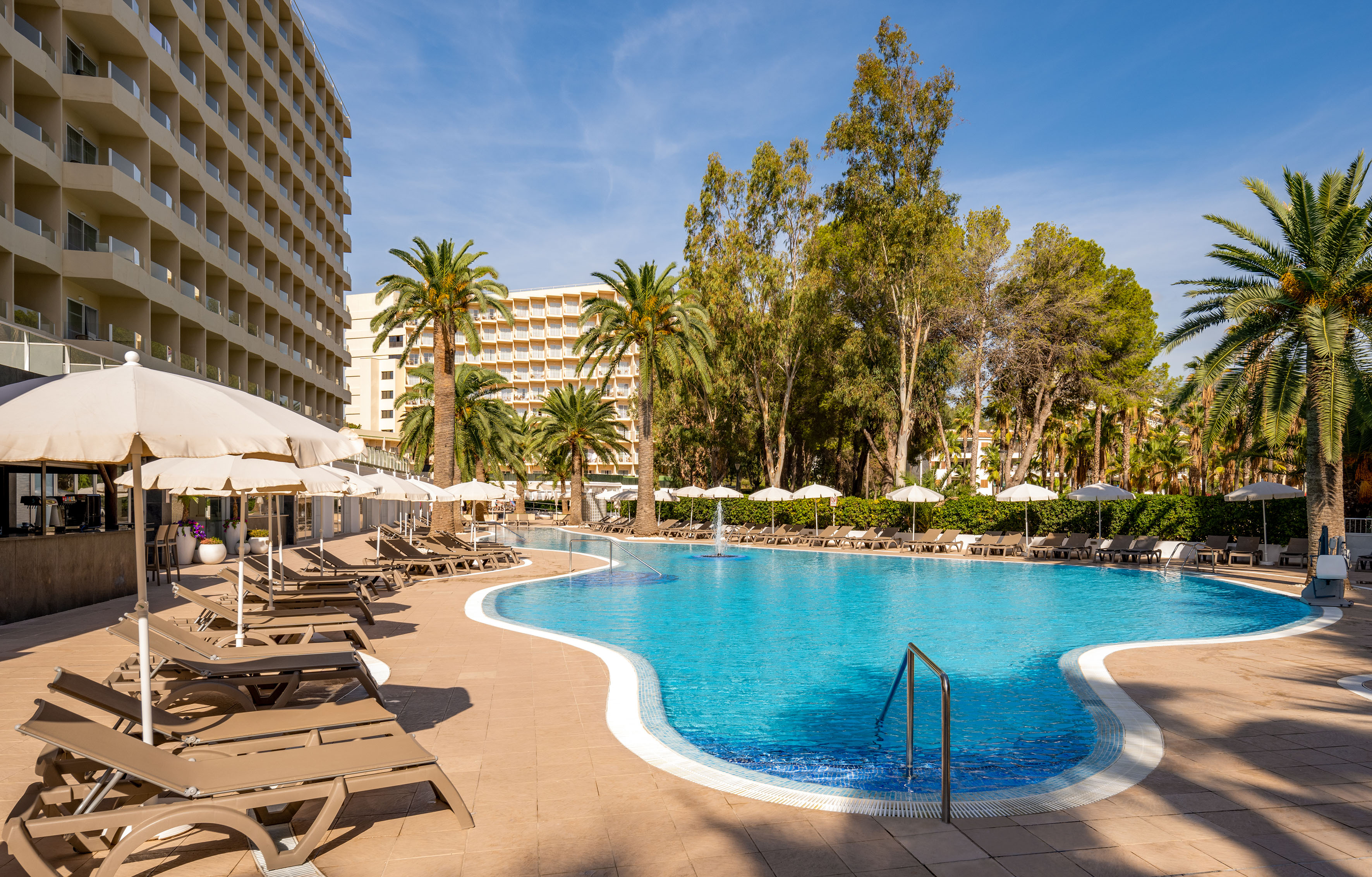 a pool with lounge chairs and umbrellas in front of a building
