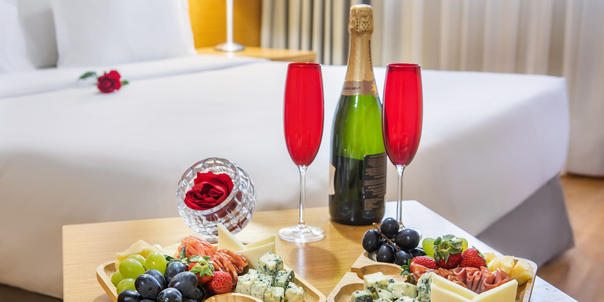 Hotel room with charcuterie board, champagne, red flutes, and roses.