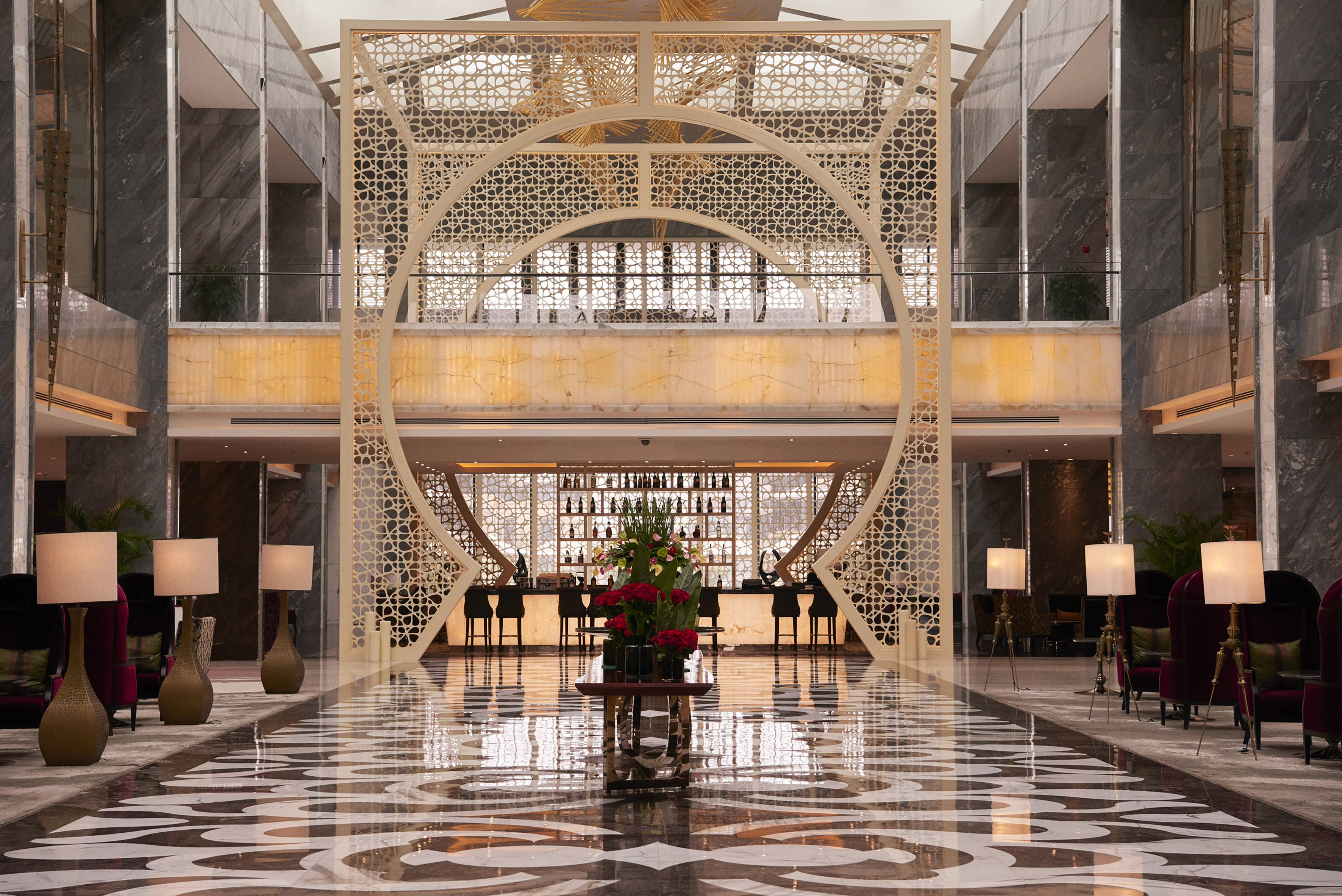 Elegant hotel lobby with ornate screen, reflective marble floor, and sophisticated bar lounge.