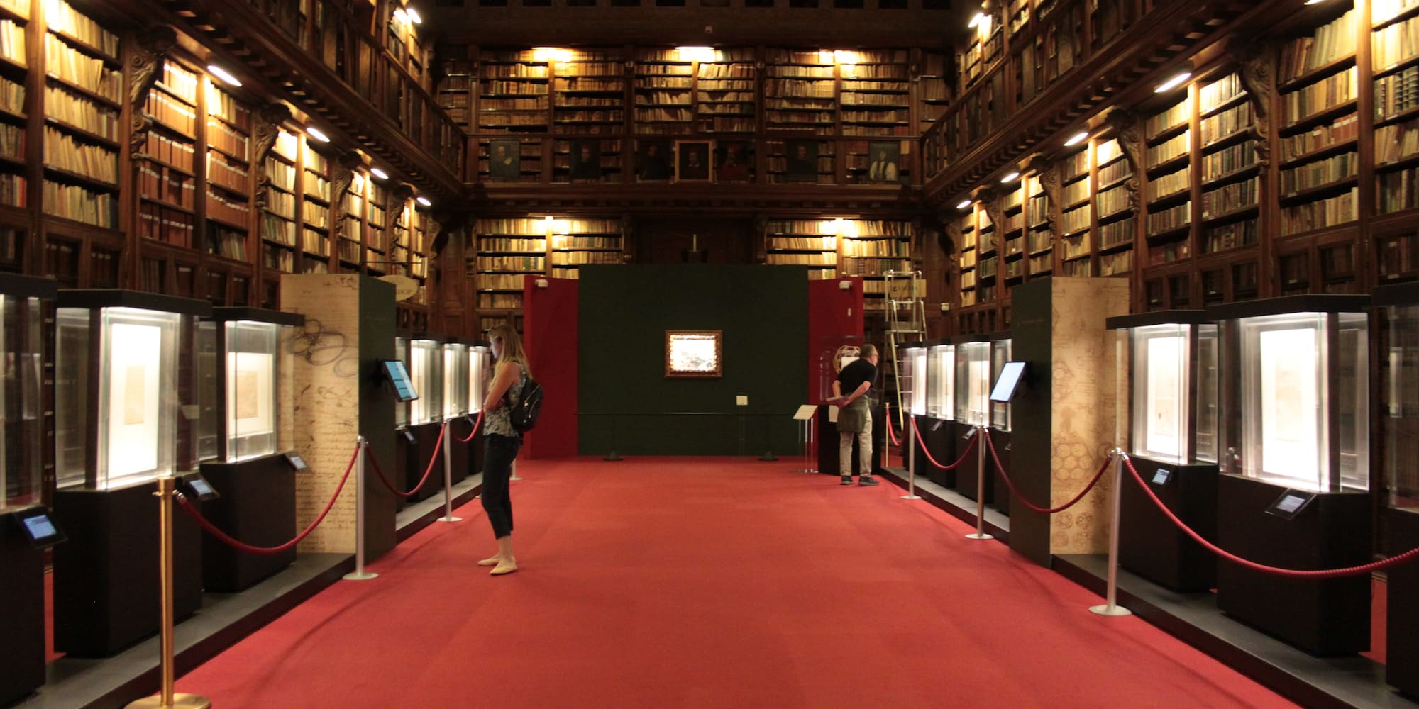 people in a library with red carpet and red rope barriers