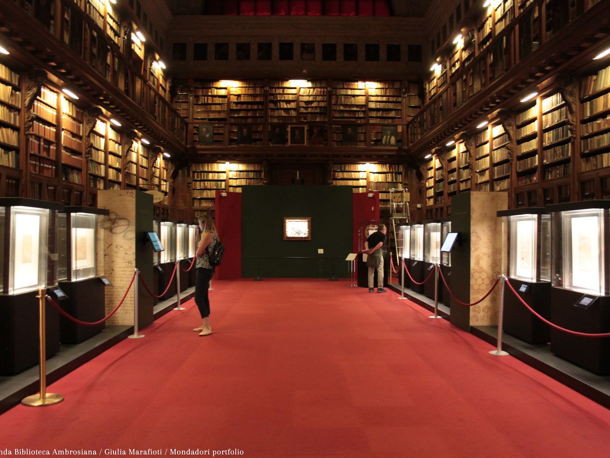 people in a library with red carpet and red rope barriers