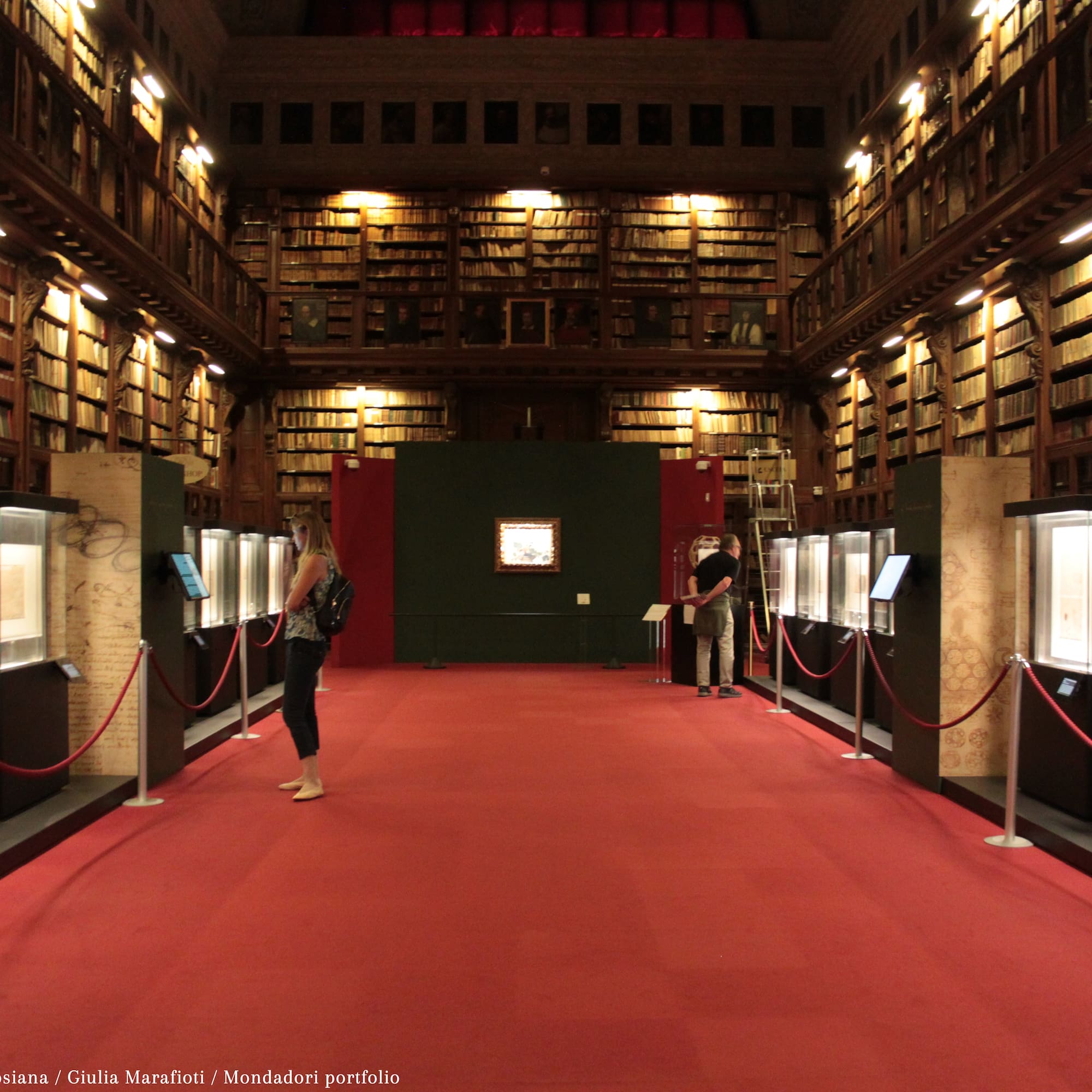 people in a library with red carpet and red rope barriers