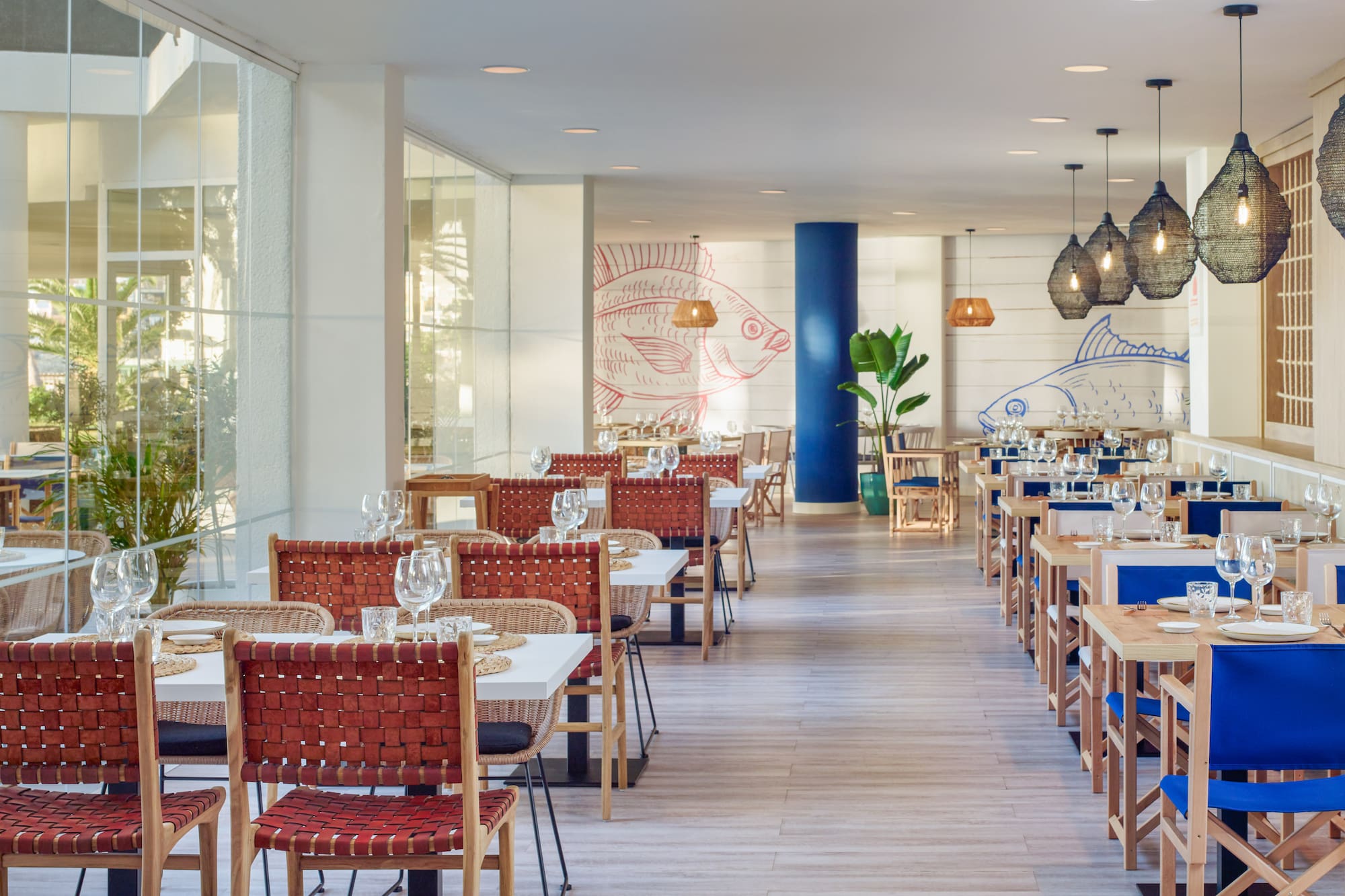 Coastal restaurant dining room with fish murals, woven chairs, and large windows.