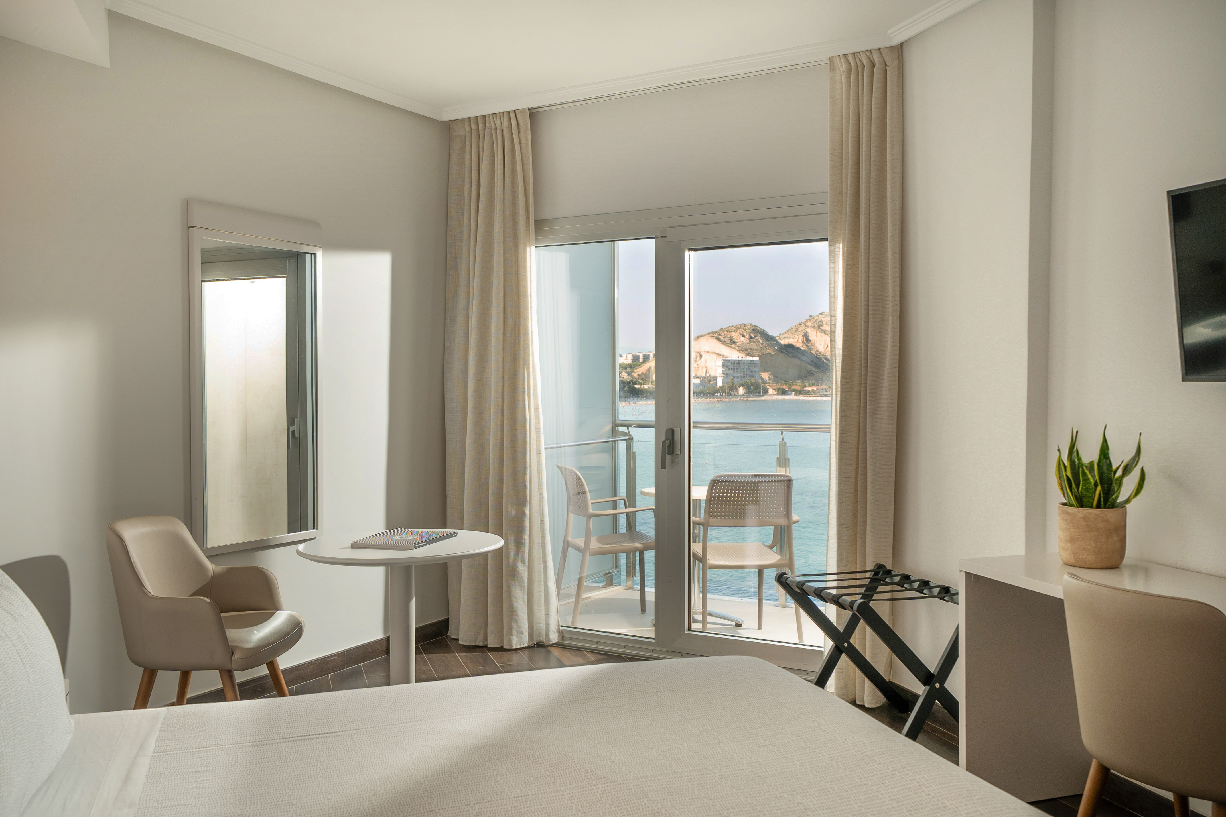 Hotel room with sea view balcony, bed, and mountain landscape.