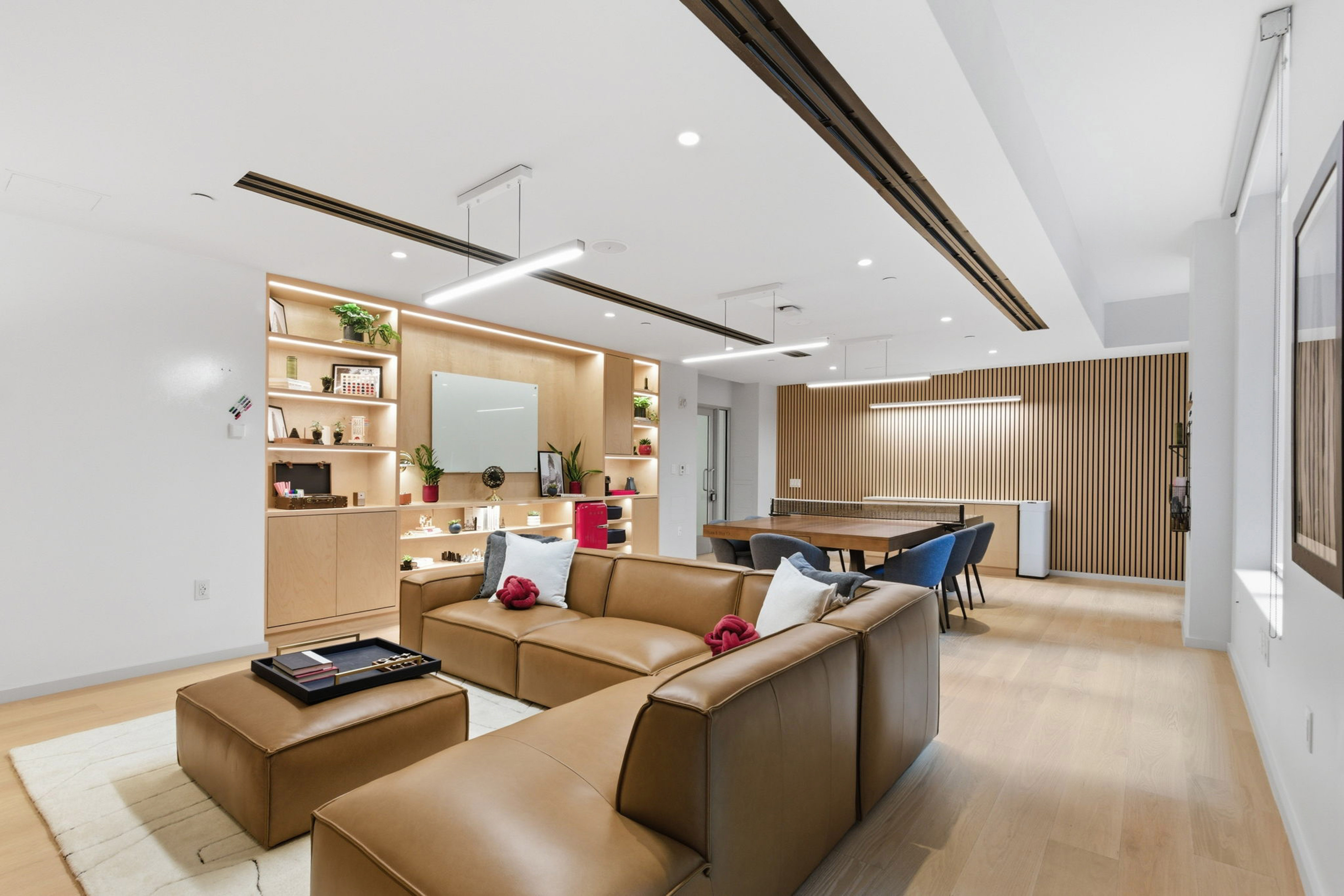 Modern lounge area with brown leather sofa, wood shelves, meeting table, ping pong.
