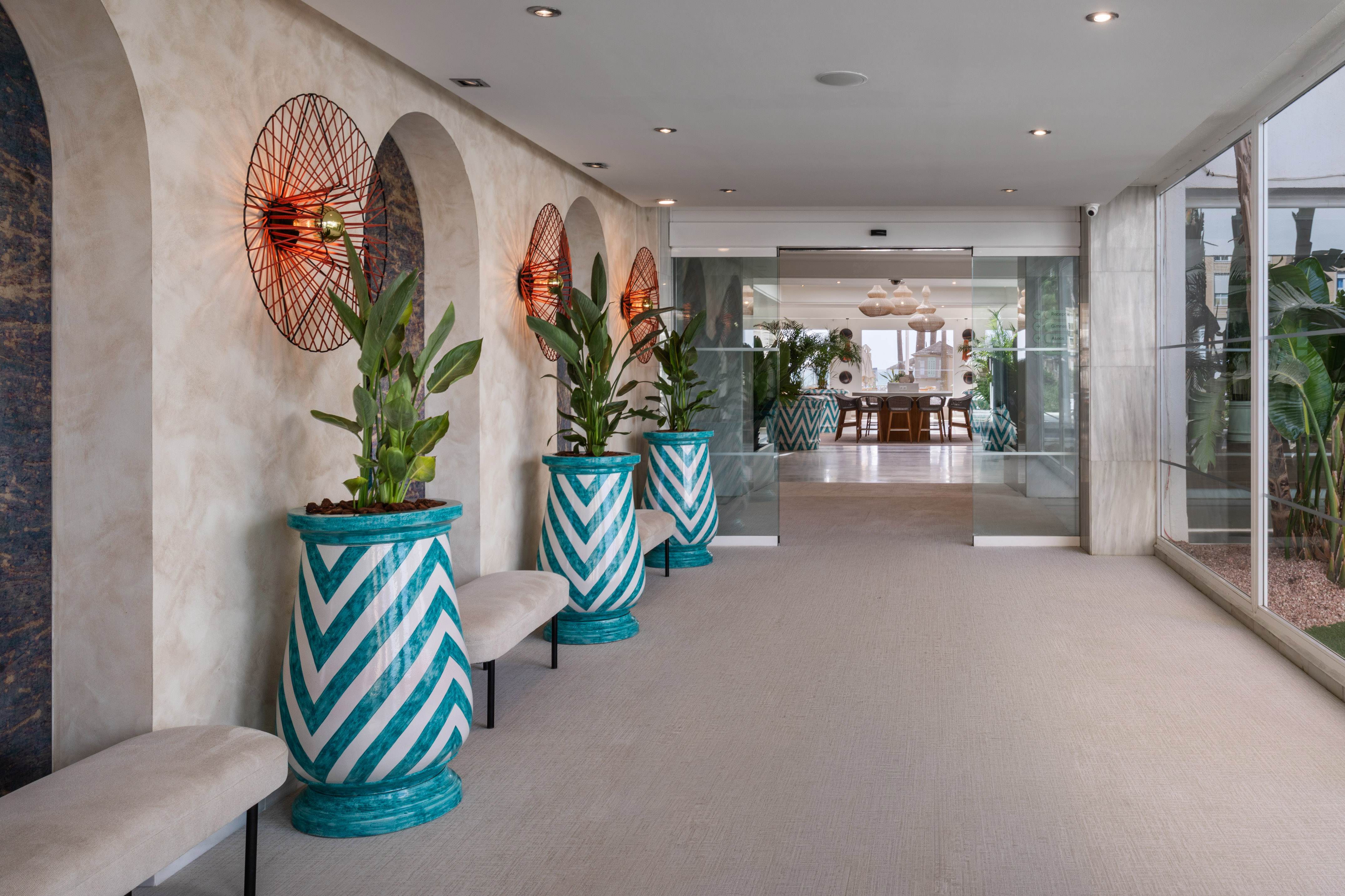Resort hallway with archways, sunburst lights, and plants in blue chevron pots.