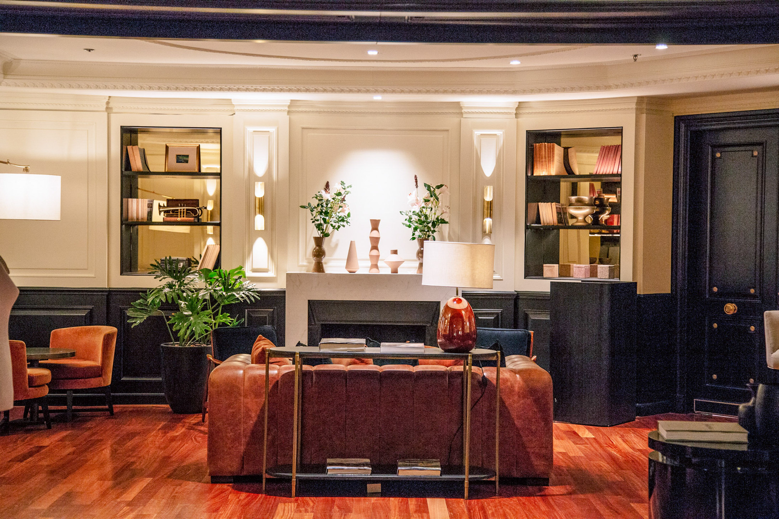Salón de hotel clásico con sofá de cuero, chimenea, estanterías y piso de madera.