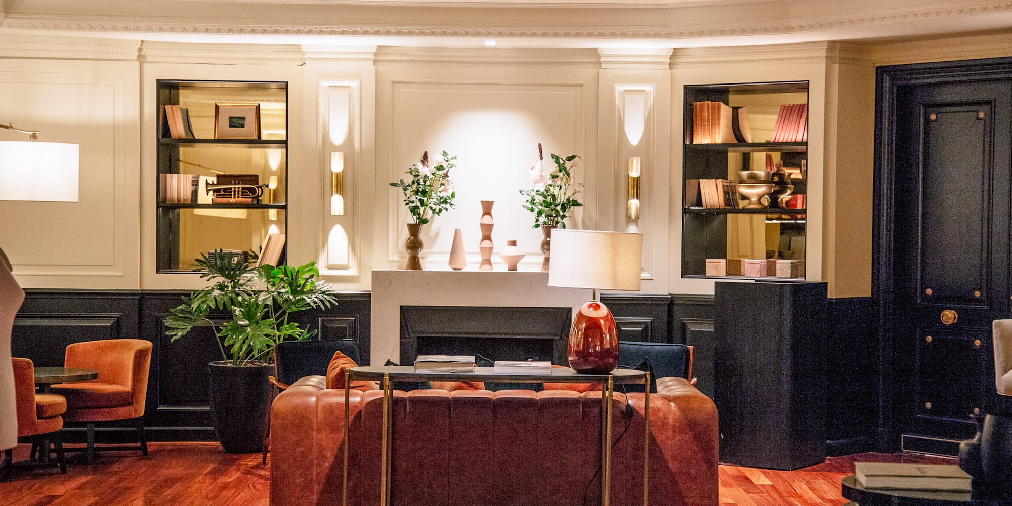 Salón de hotel clásico con sofá de cuero, chimenea, estanterías y piso de madera.