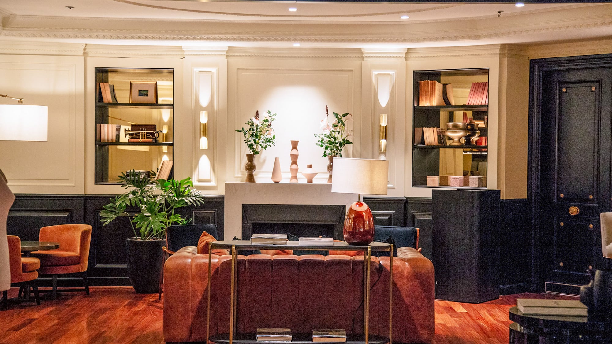 Salón de hotel clásico con sofá de cuero, chimenea, estanterías y piso de madera.
