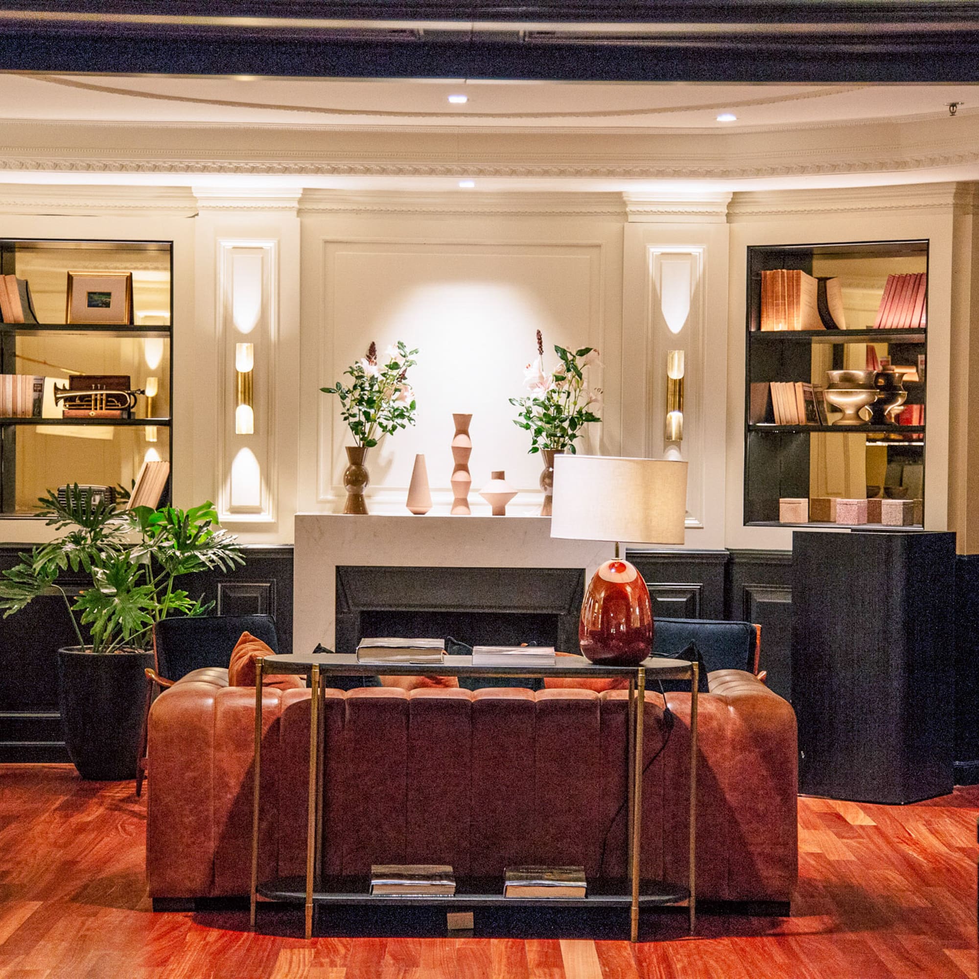 Salón de hotel clásico con sofá de cuero, chimenea, estanterías y piso de madera.