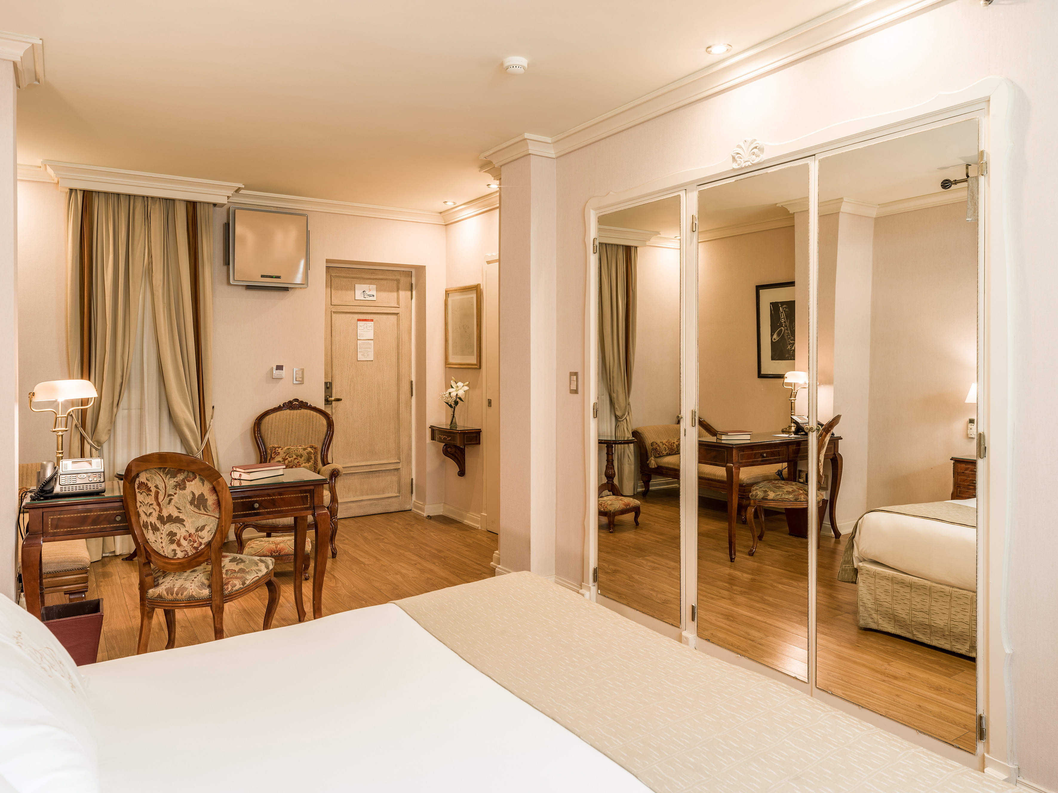 Elegant hotel room with mirrored closet, wooden desk, and classic decor.