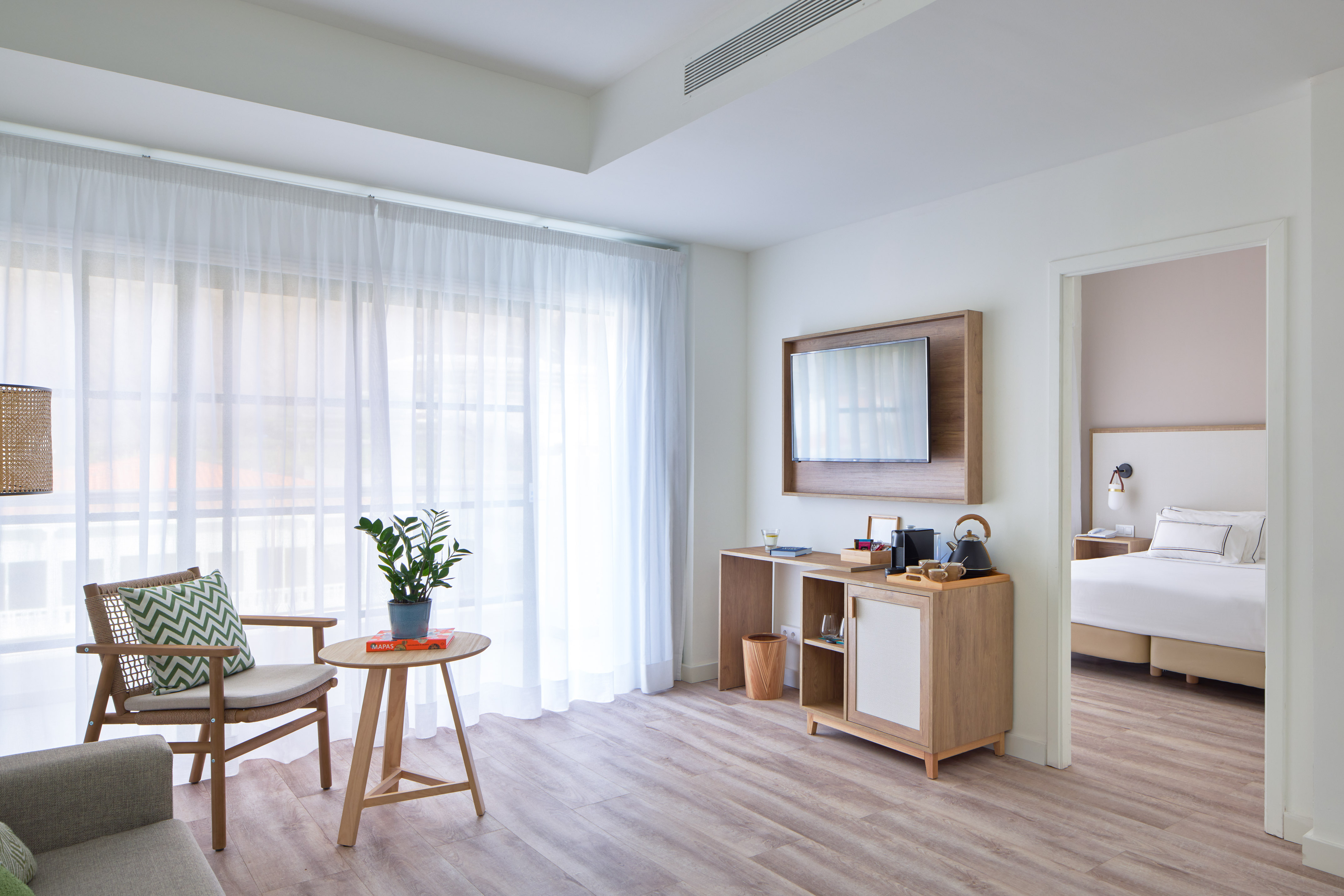 Modern hotel suite: living area with wood furniture, coffee bar, and bedroom.