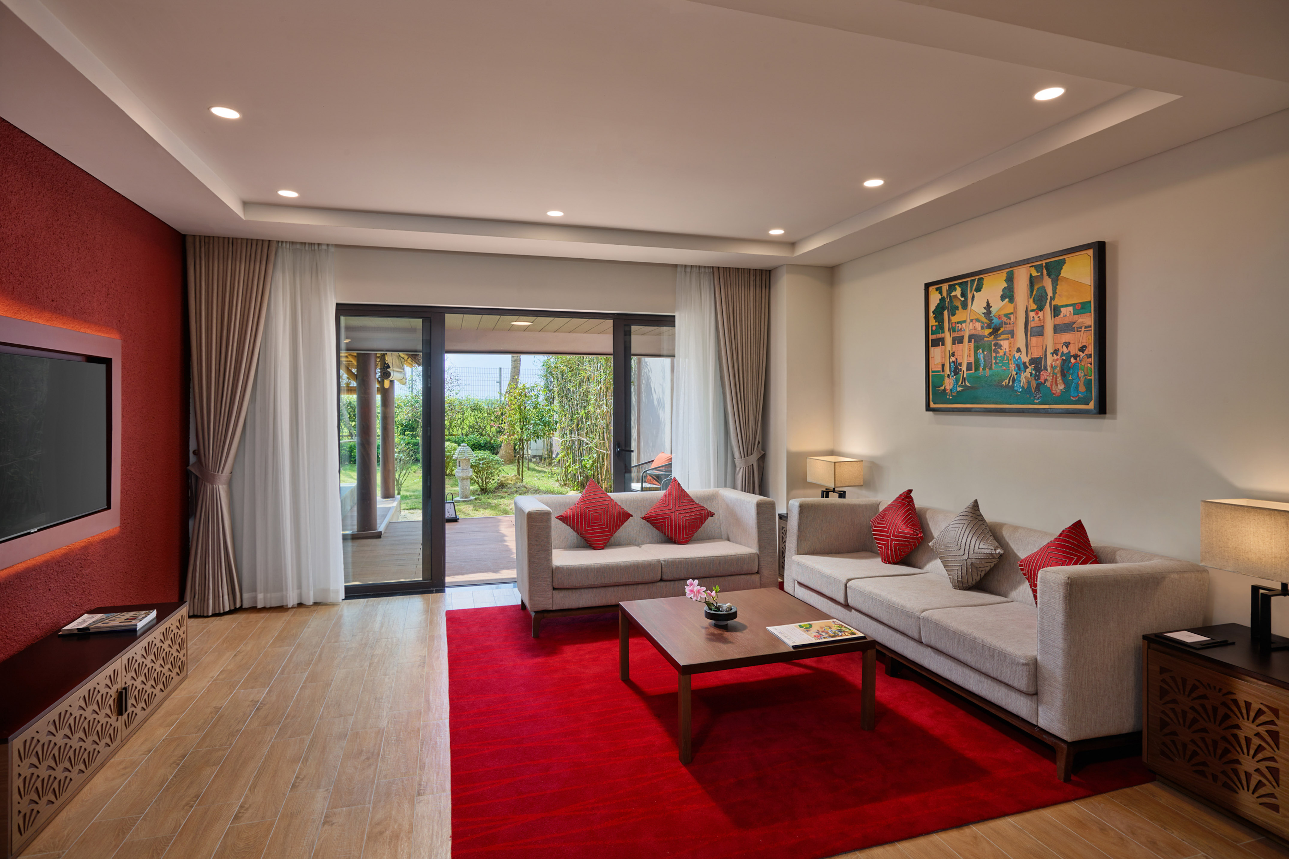 Modern living room with light sofas, red rug, and garden view from glass doors.