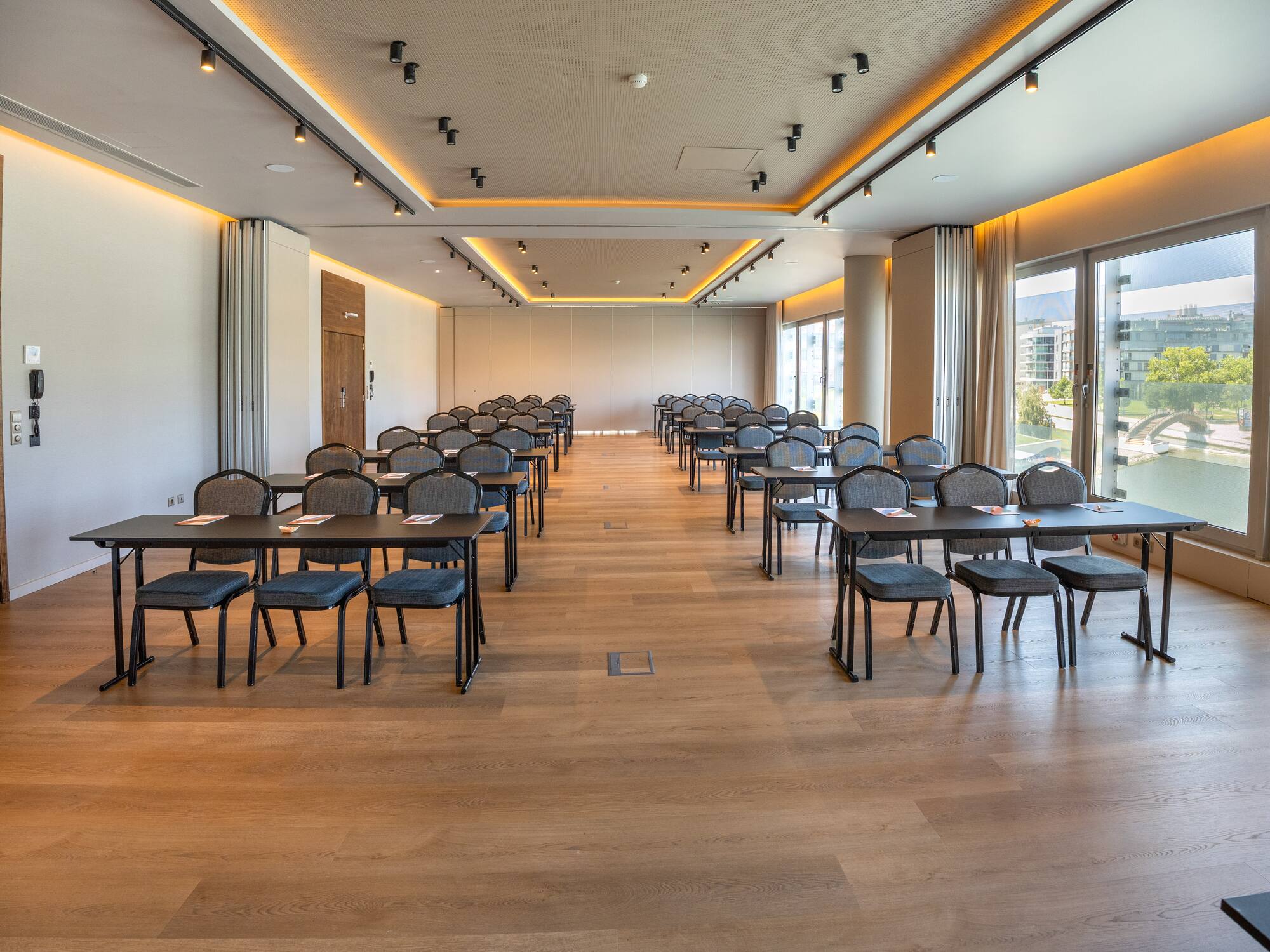 Modern conference room with tables, chairs, wood floor, and large windows.
