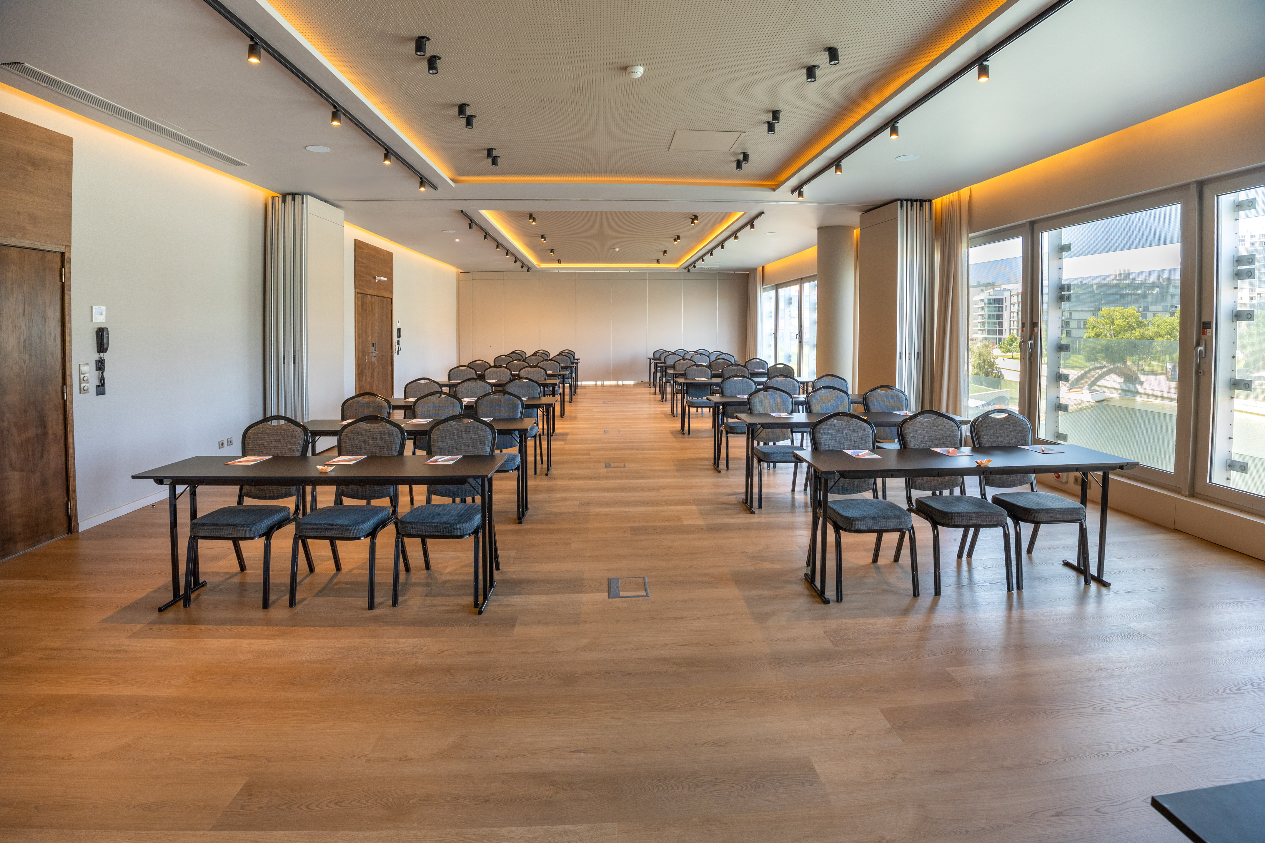 Modern conference room with tables, chairs, wood floor, and large windows.