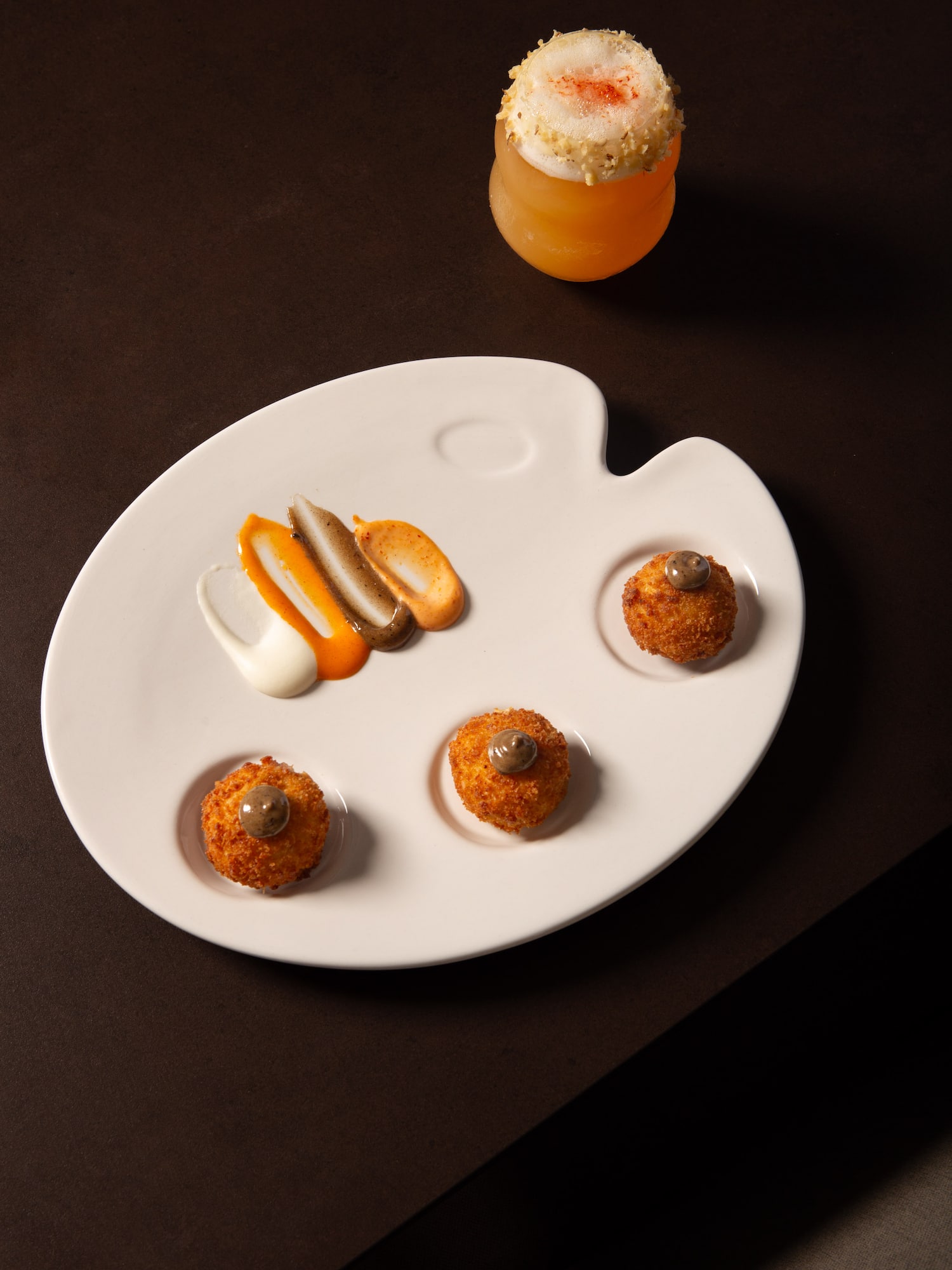 Gourmet croquettes, sauces on a palette plate, and a frothy cocktail.