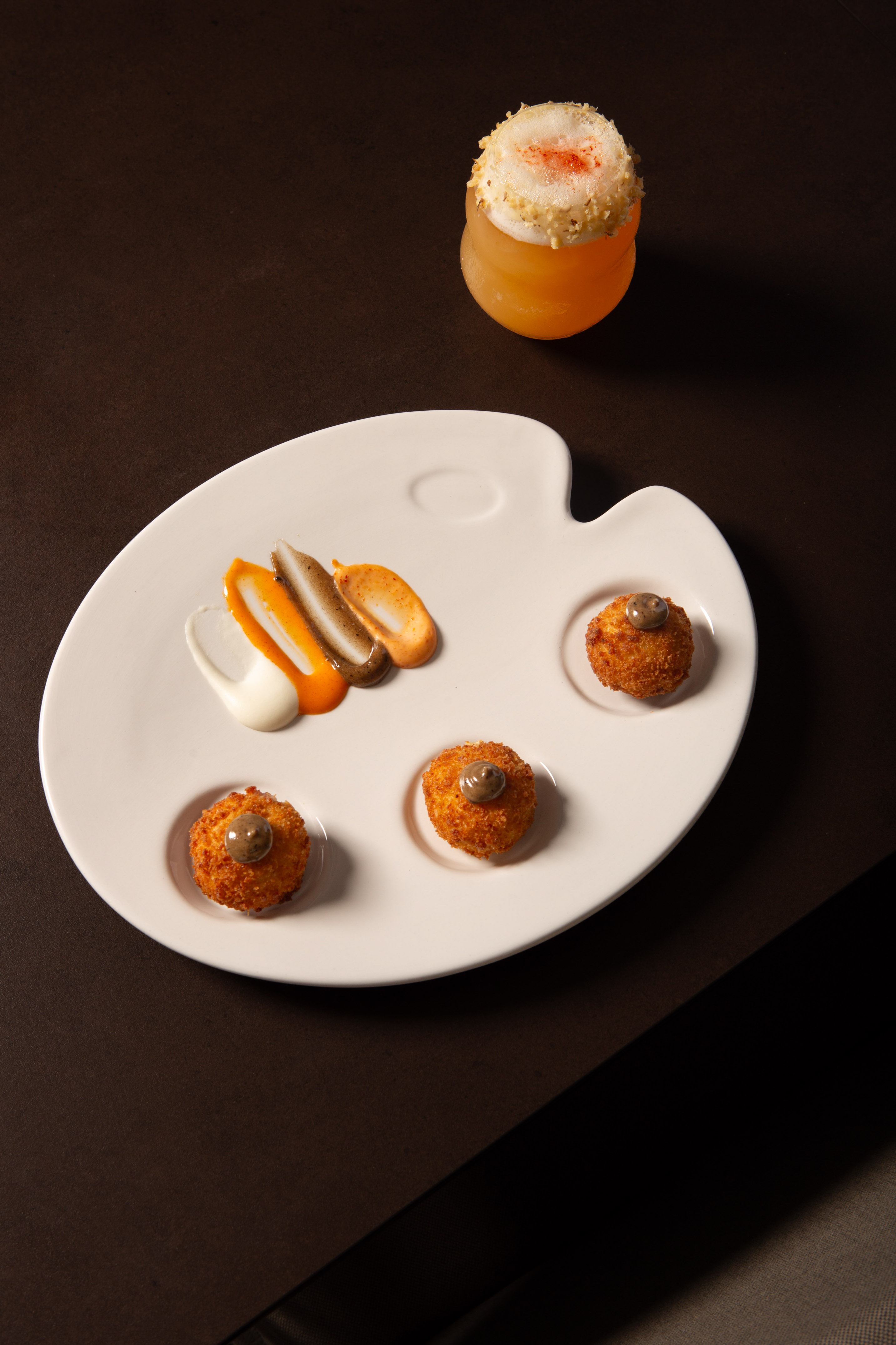 Gourmet croquettes, sauces on a palette plate, and a frothy cocktail.