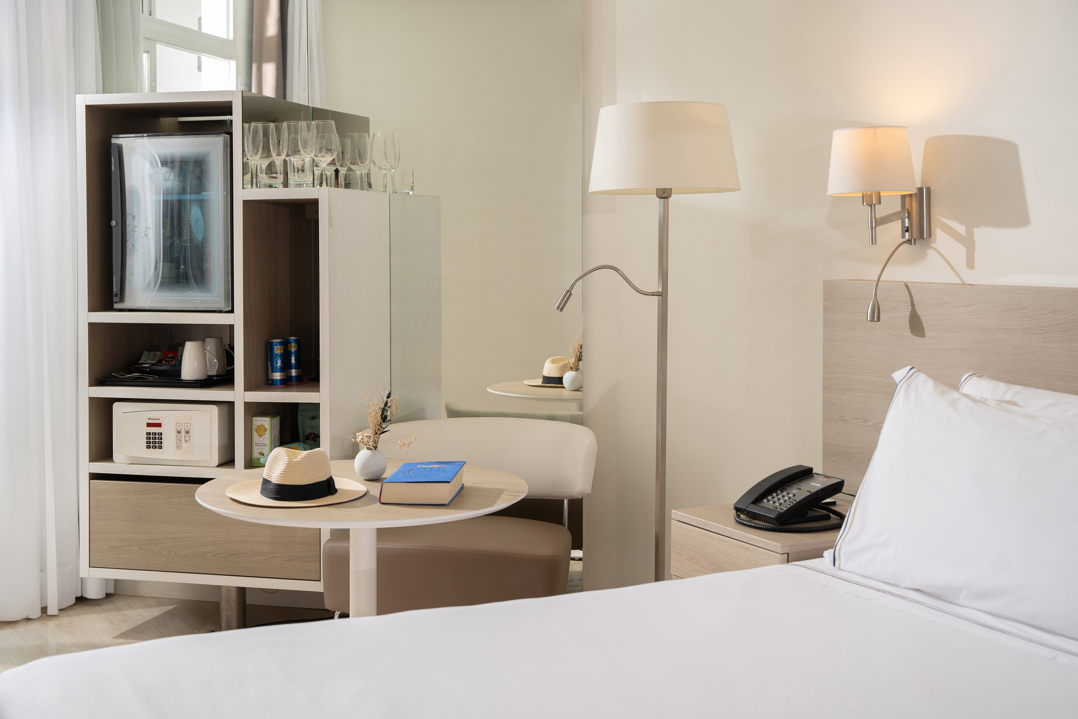 Modern hotel room with bed, mini-bar, safe, and cozy seating area.