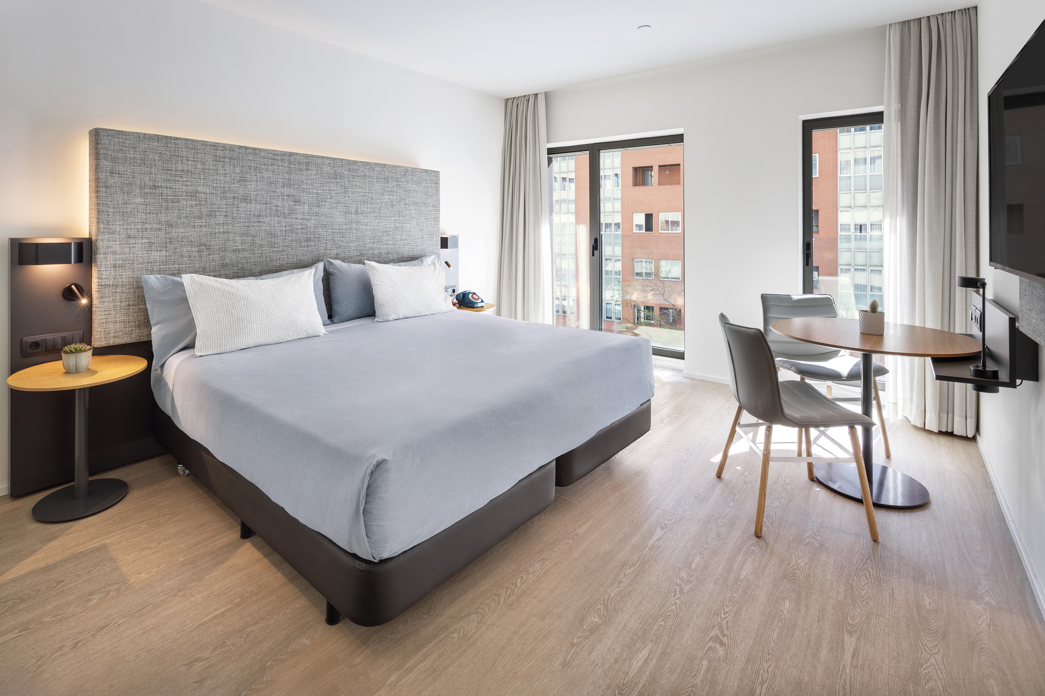 Modern studio apartment with king bed, work table, and city view window.