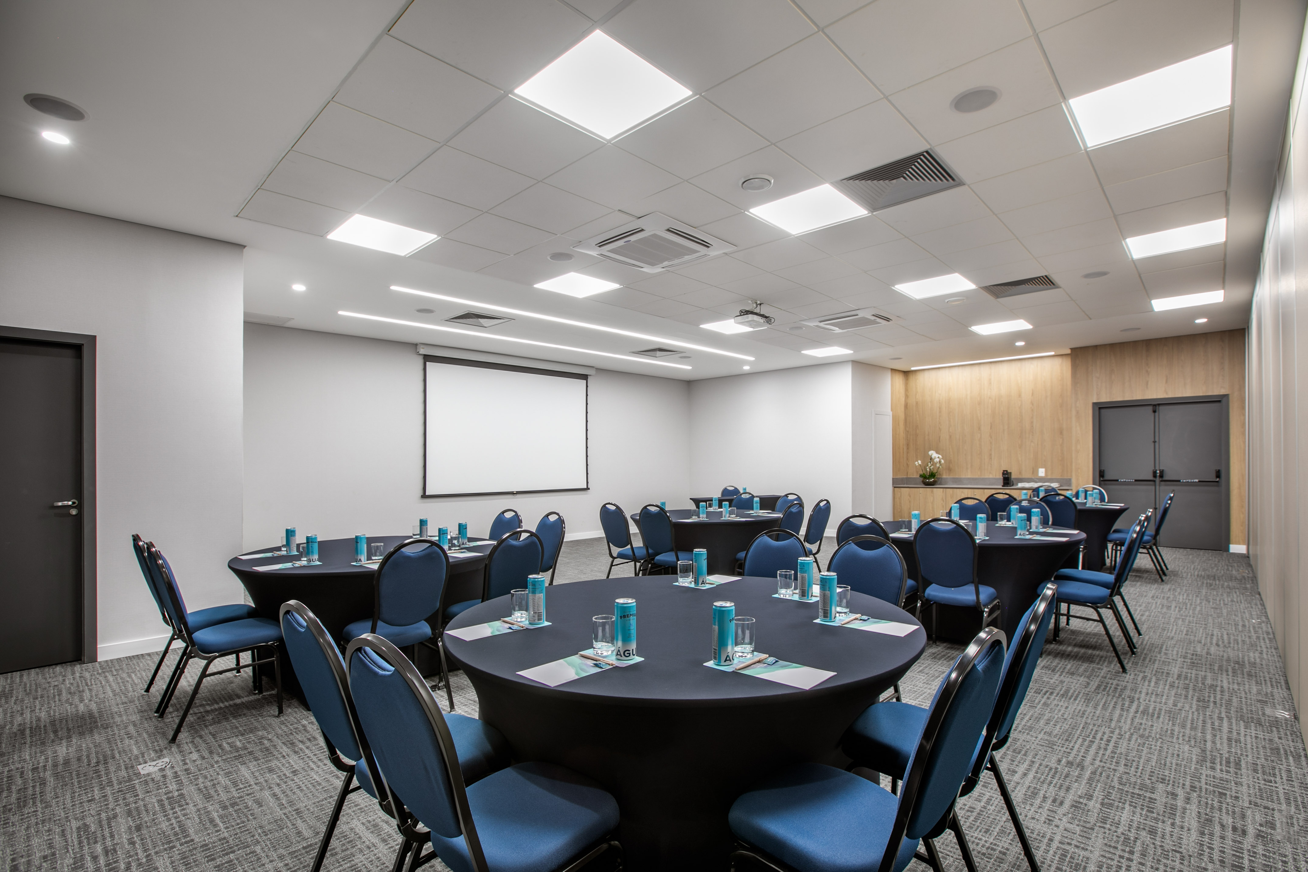 Modern meeting room setup with round tables, blue chairs, and projector screen.
