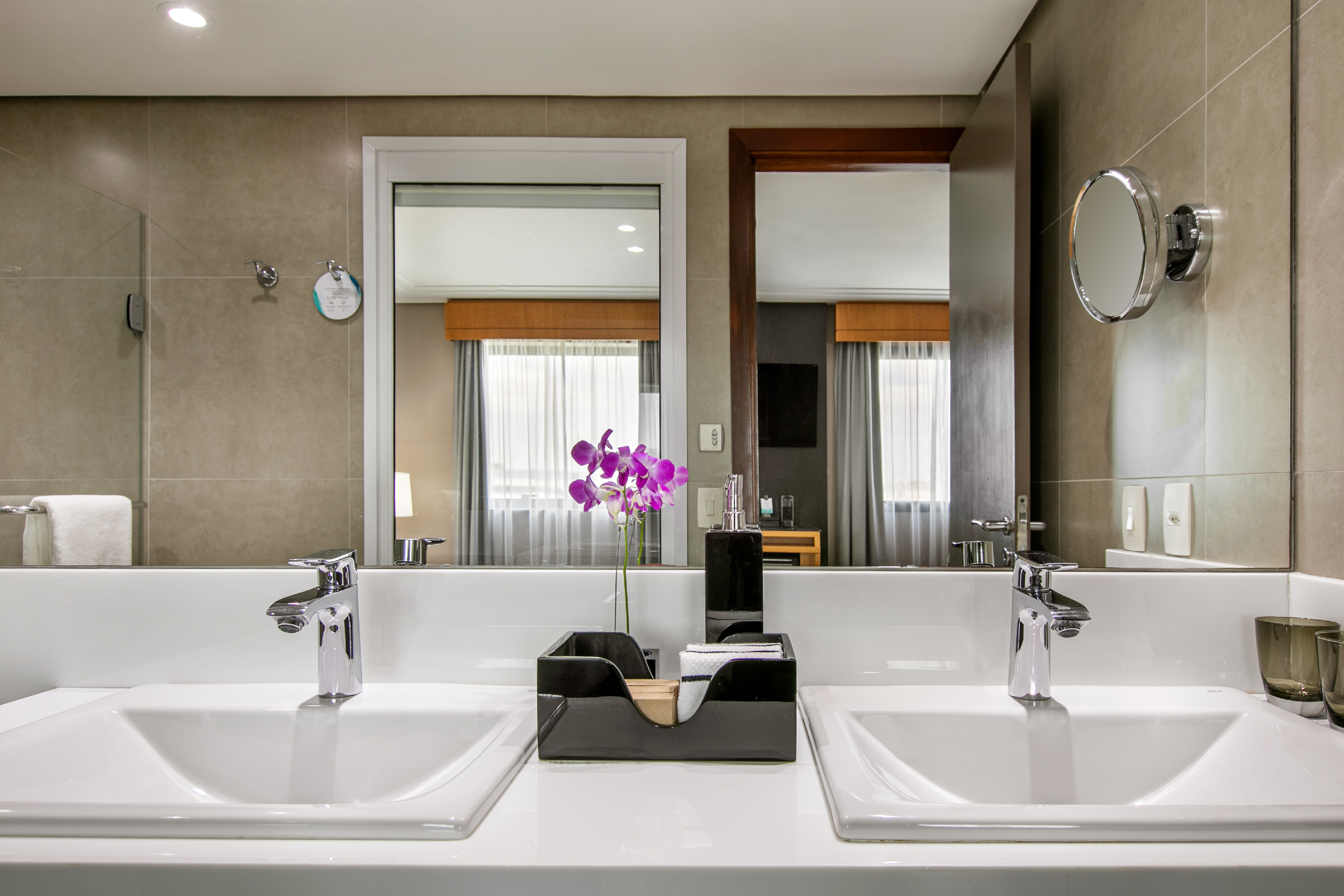 Modern hotel bathroom with double vanity, white sinks, and purple orchid decoration.
