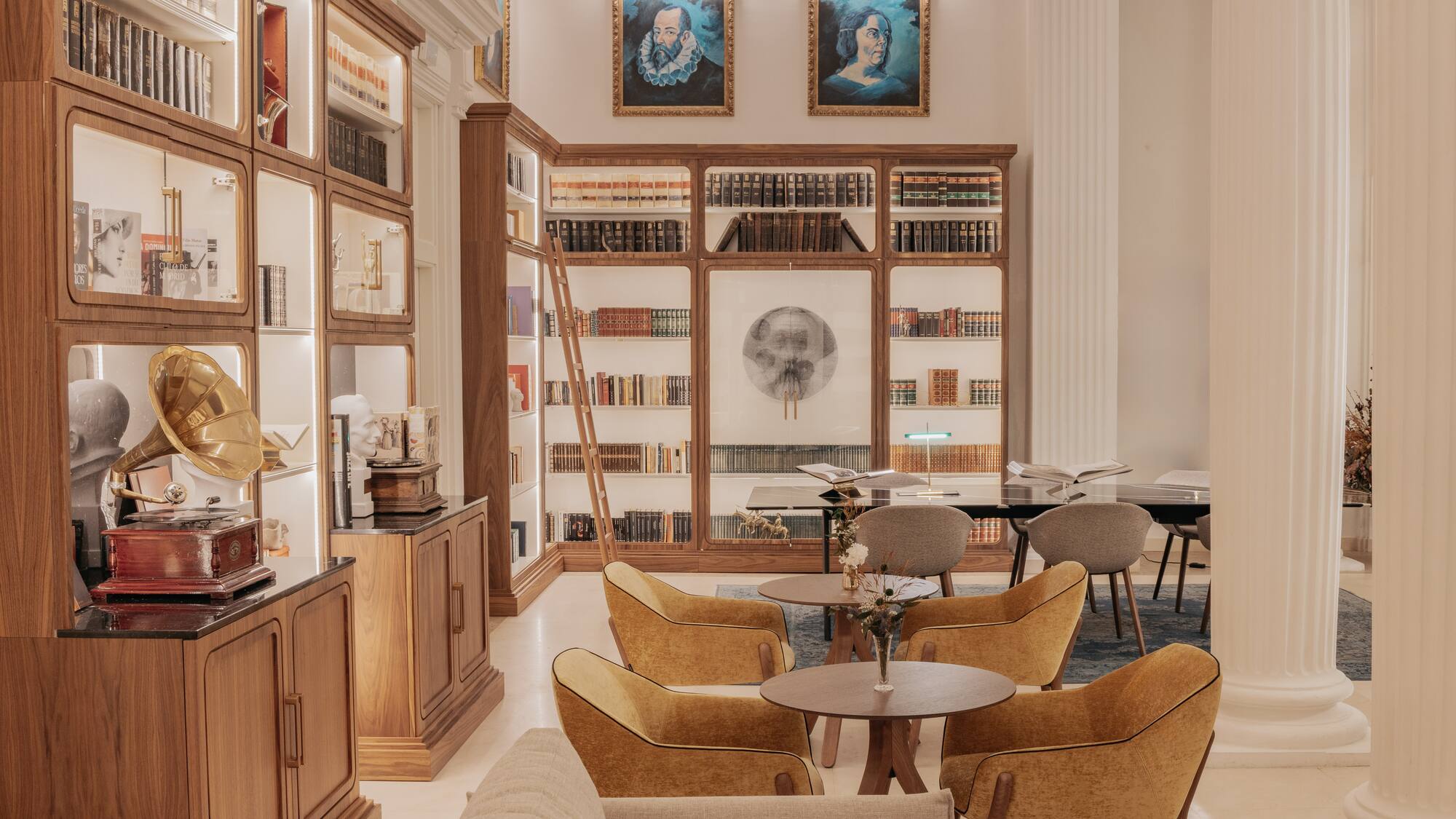 Library lounge with wooden bookshelves, vintage gramophone, portraits, and comfortable seating.
