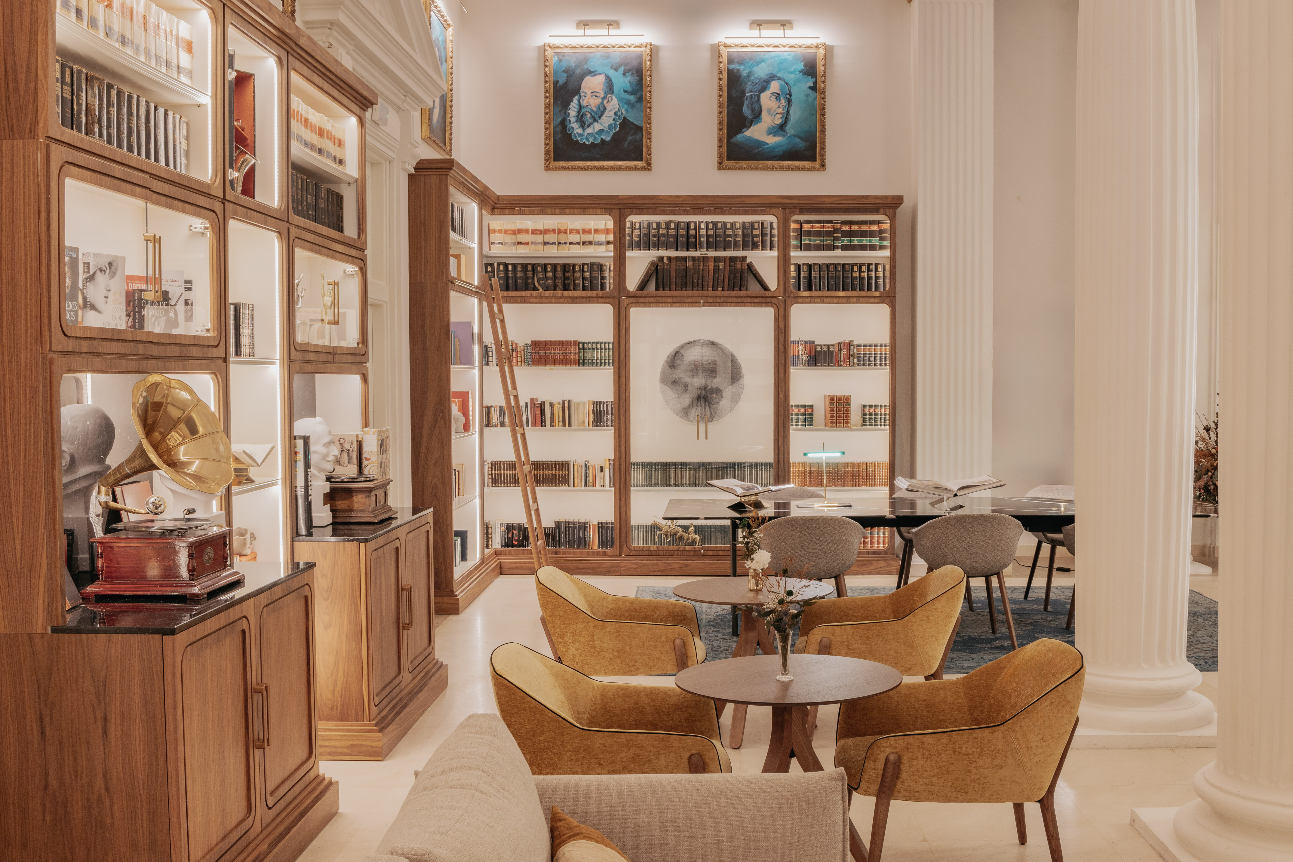 Library lounge with wooden bookshelves, vintage gramophone, portraits, and comfortable seating.