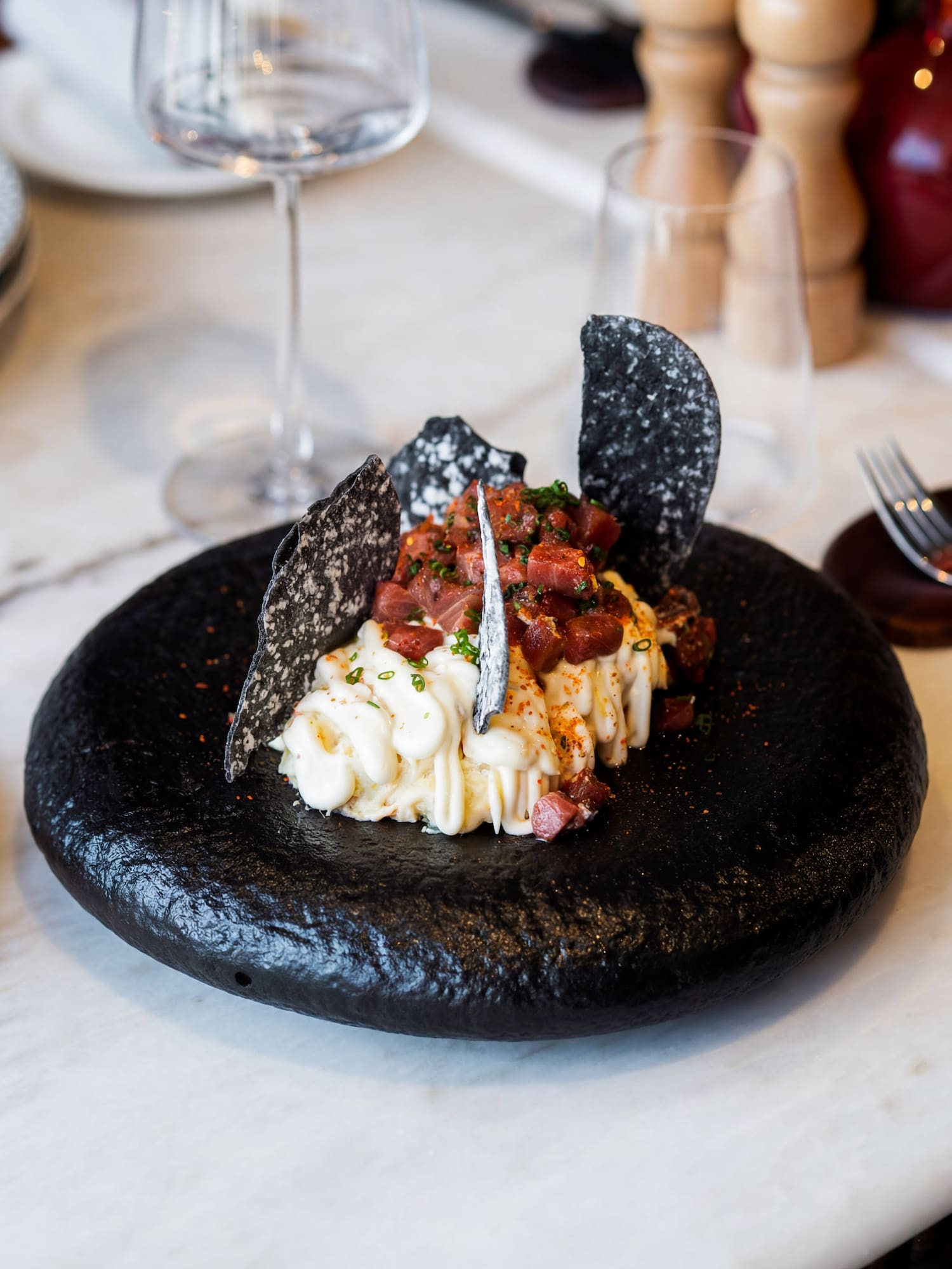 Fresh tuna tartare, creamy sauce, black crackers on a textured black plate.