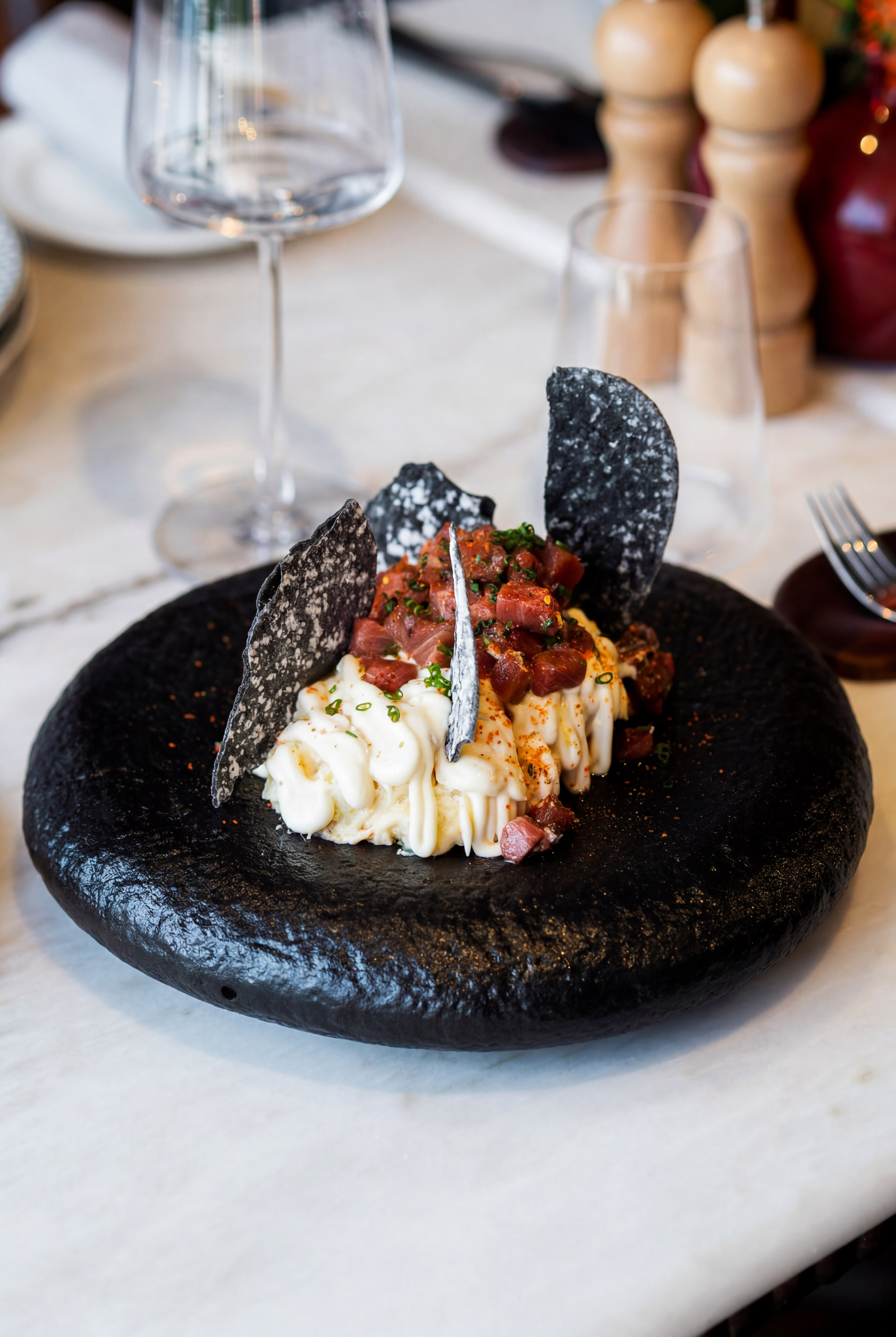 Fresh tuna tartare, creamy sauce, black crackers on a textured black plate.
